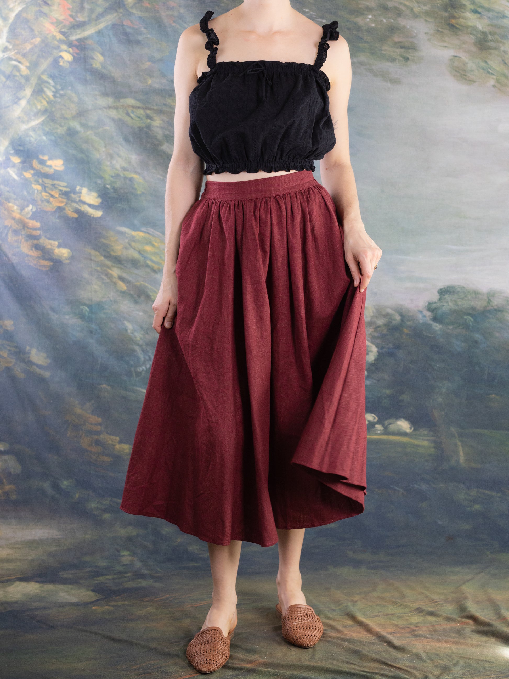 Woman wearing a black Lacey Chemisette Tank paired with a red skirt and woven slip-on shoes against a painted backdrop