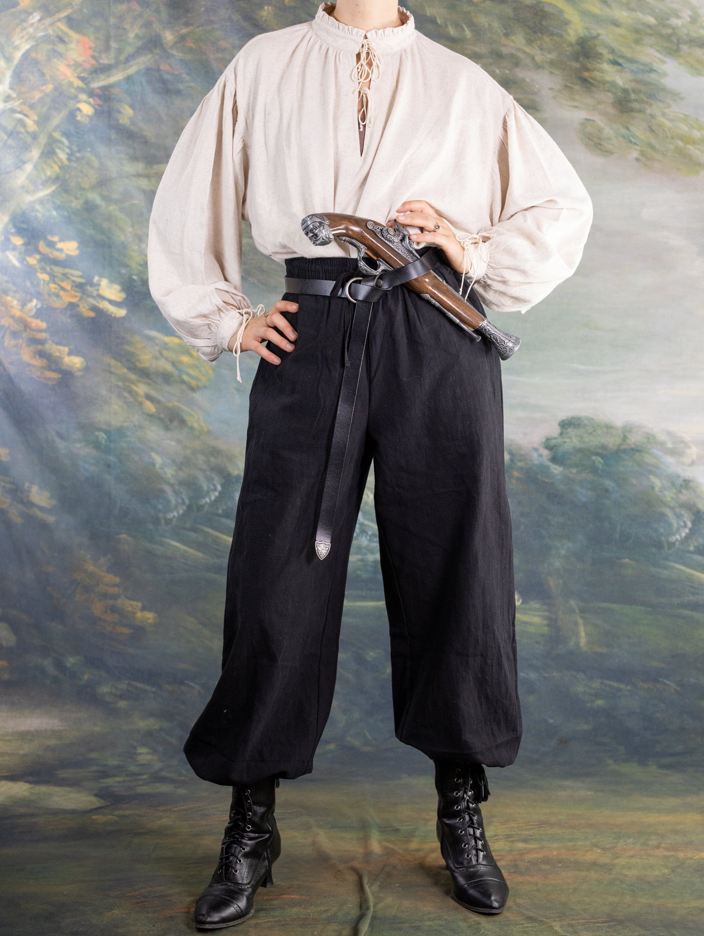 Person wearing black rustic Pirate Pants with a white medieval-style shirt and leather belt holding a prop pistol