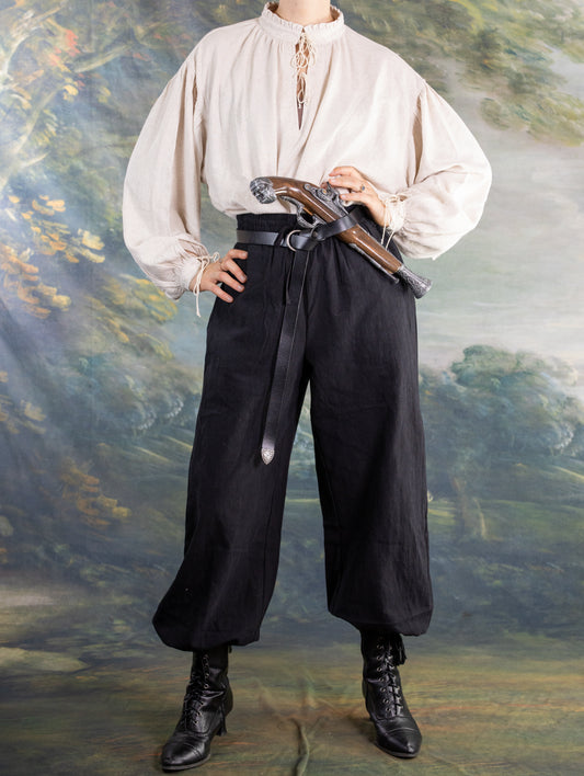 Person wearing black rustic Pirate Pants with a white medieval-style shirt and leather belt holding a prop pistol