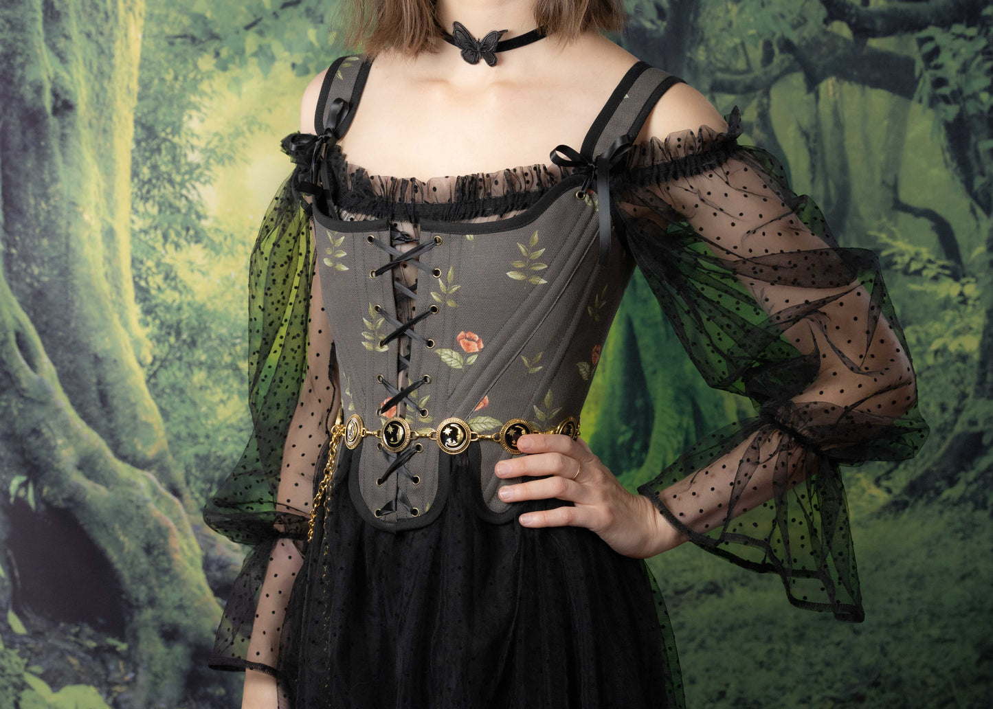 Woman wearing Handmade Black Rose Floral 18th Century Stays with sheer polka dot sleeves and gold chain belt in forest setting