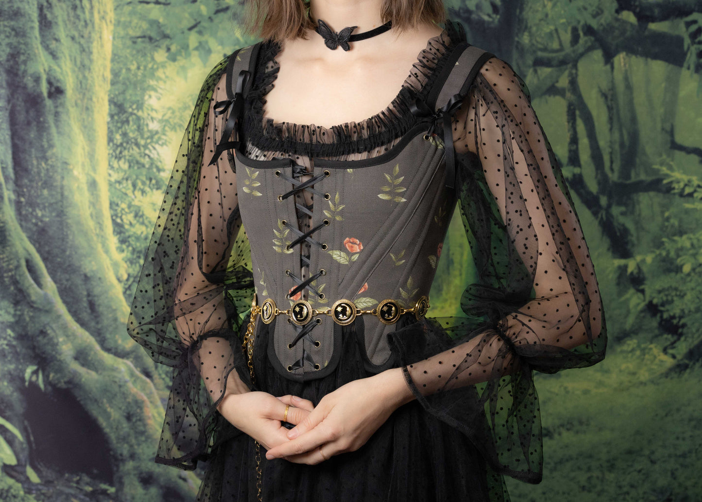 Woman wearing Handmade Black Rose Floral 18th Century Stays with sheer dotted sleeves and decorative belt in a forest setting