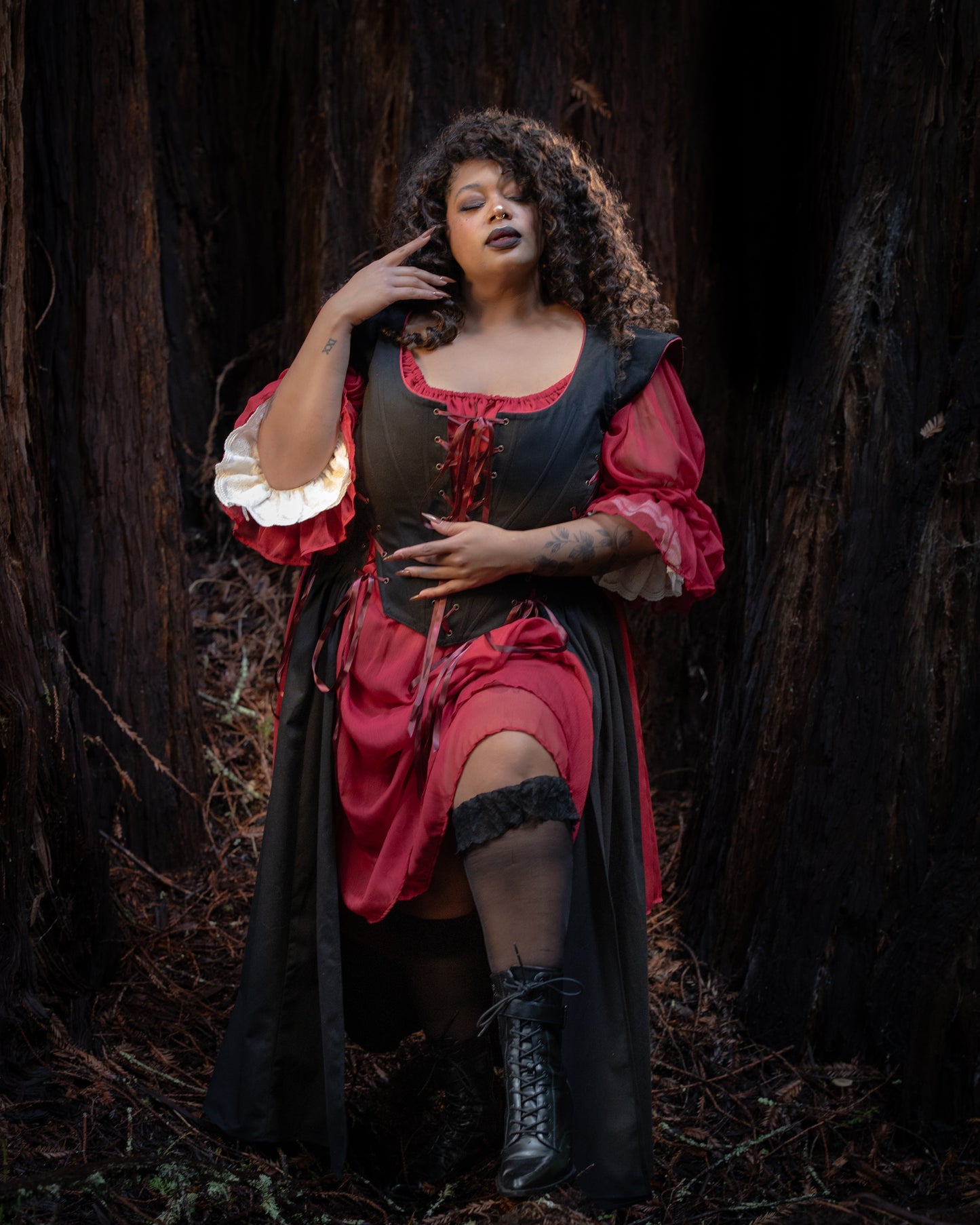 Woman posing in forest wearing a Black Vampire Slayer Corset Dress with red and white layered sleeves and black boots