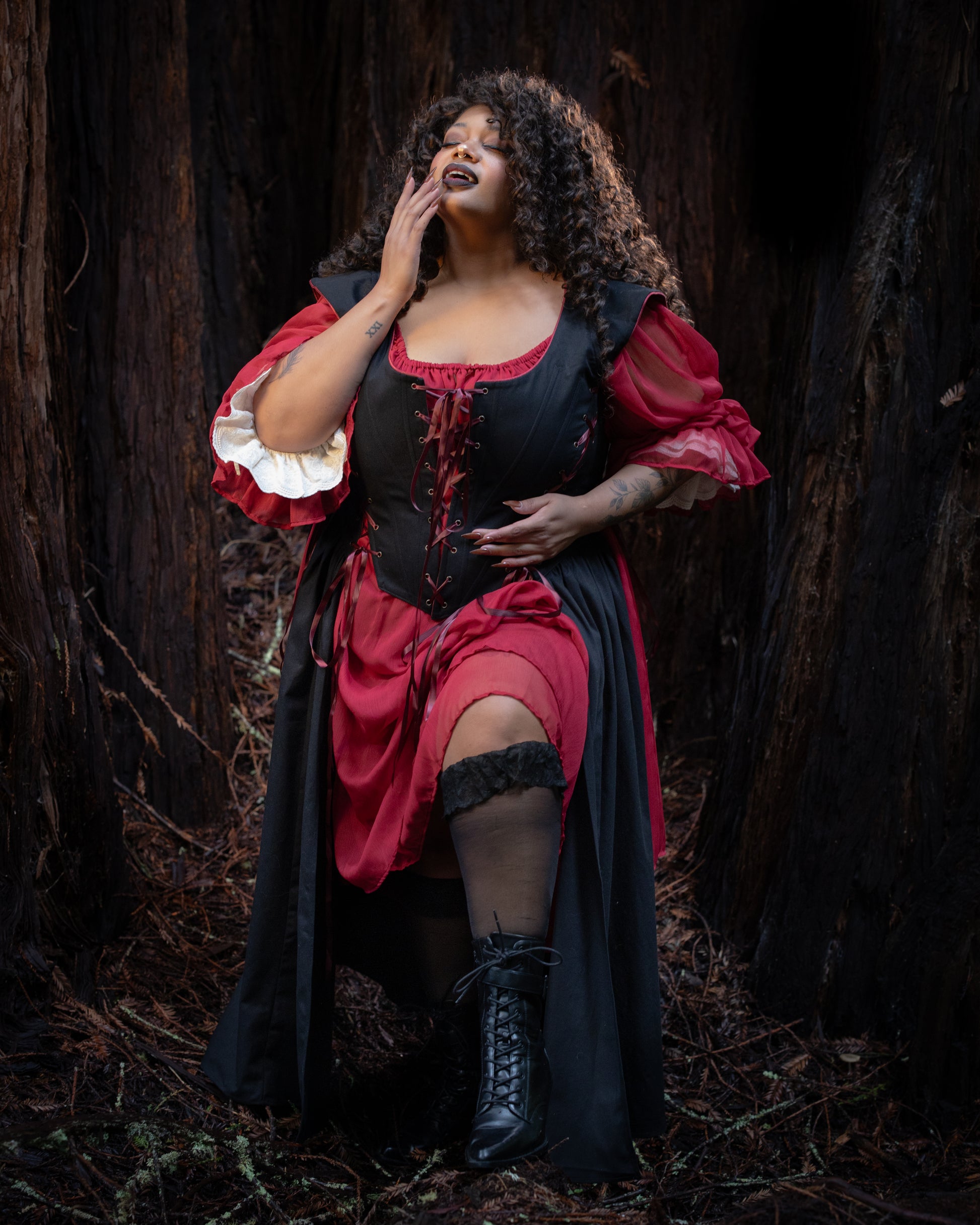 Woman posing in a dark forest wearing a Black Vampire Slayer Corset Dress with lace-up front and layered sleeves