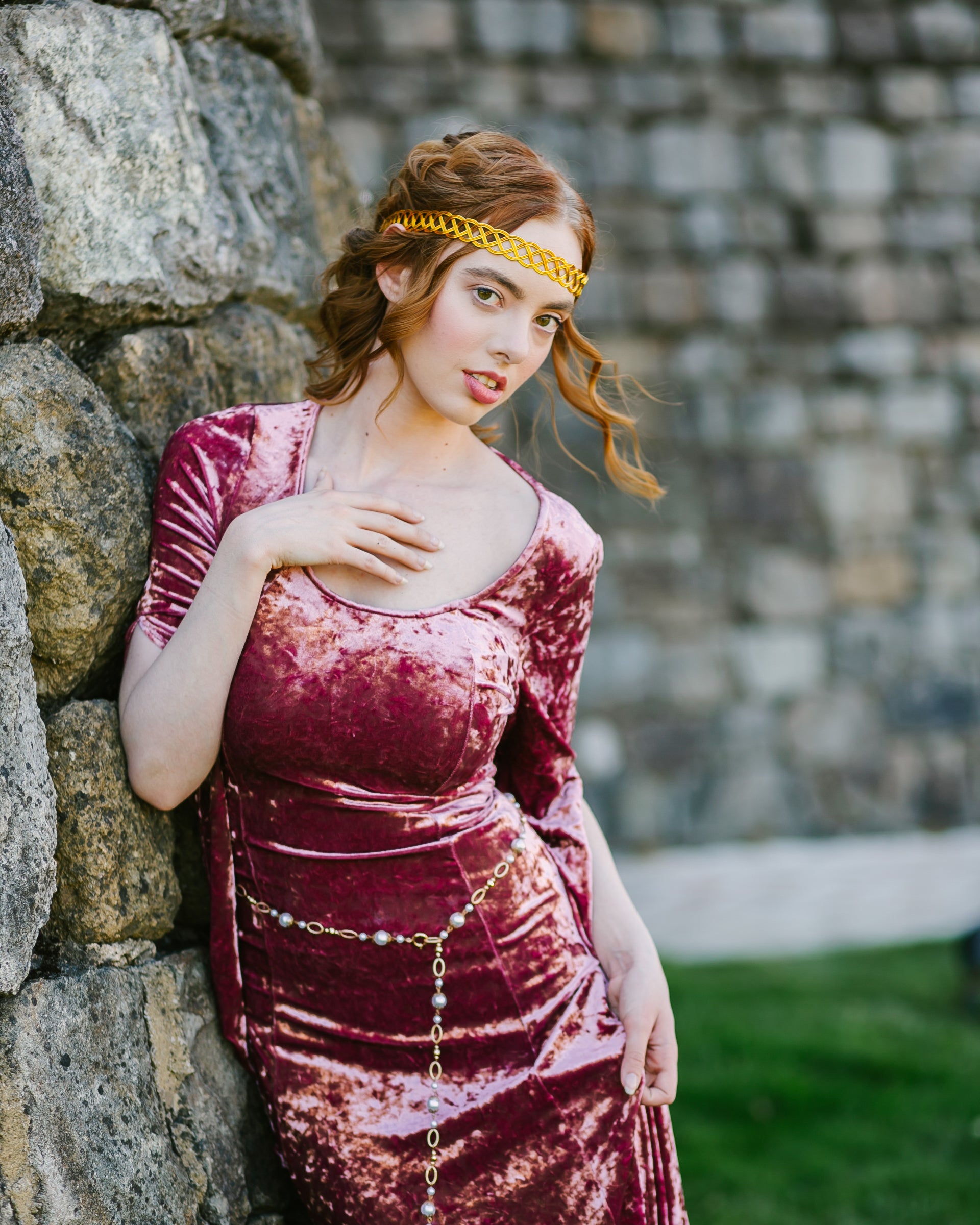 Woman in velvet dress leaning on stone wall wearing a Pearl Medieval Chain Belt with imitation pearls and metal flowers