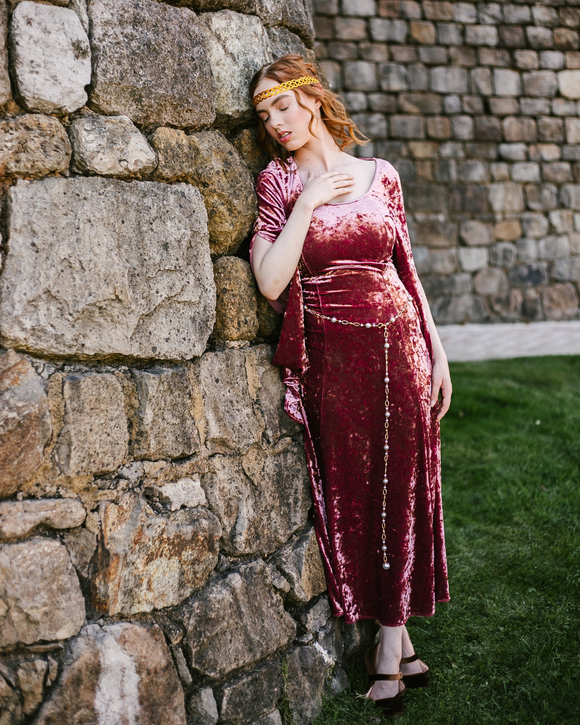 Woman in velvet medieval dress wearing a Pearl Medieval Chain Belt with imitation pearls and ornate rings standing by stone wall