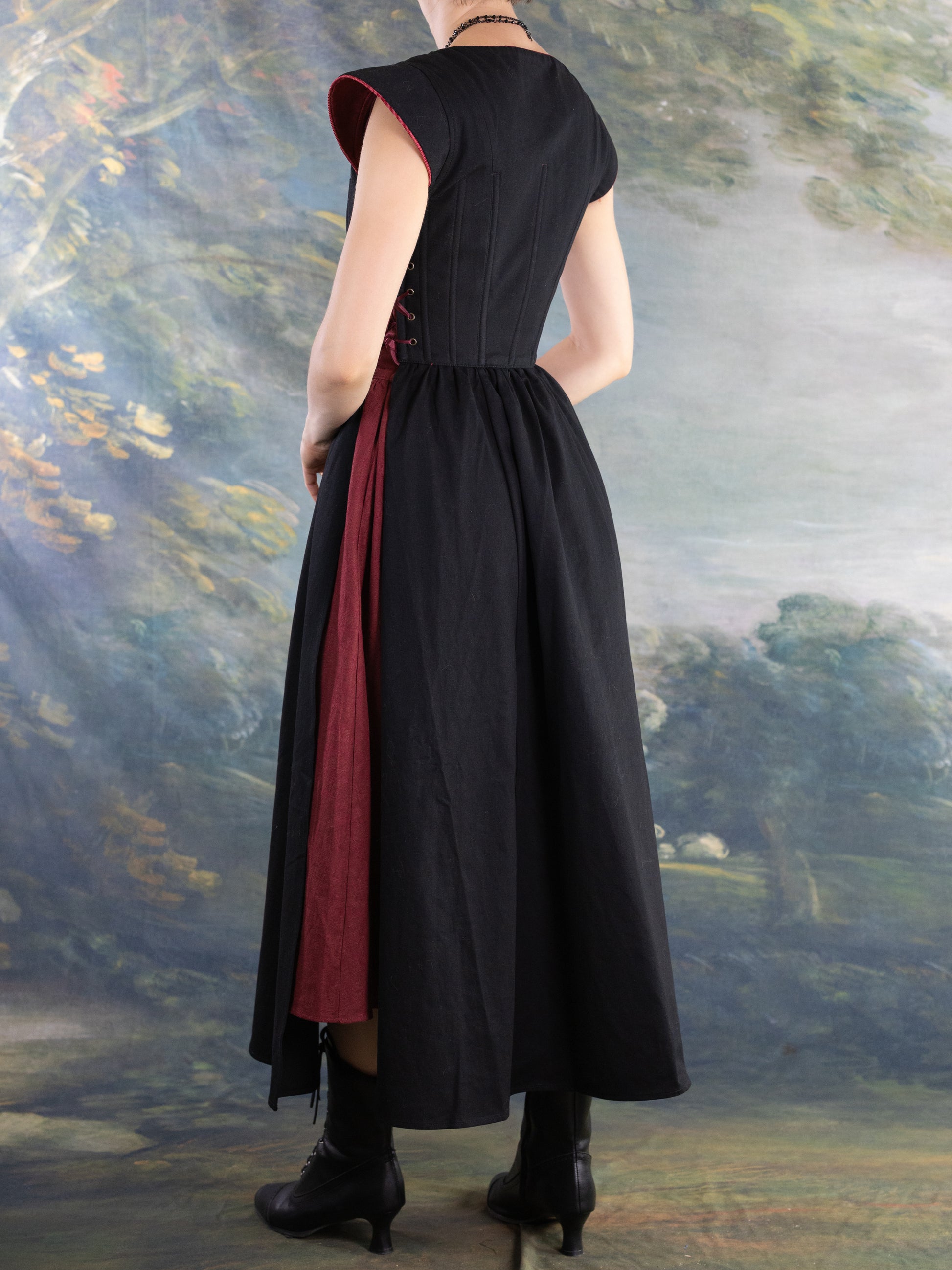 Back view of model wearing Black Vampire Slayer Corset Dress with adjustable structured bodice and dark red inner panel