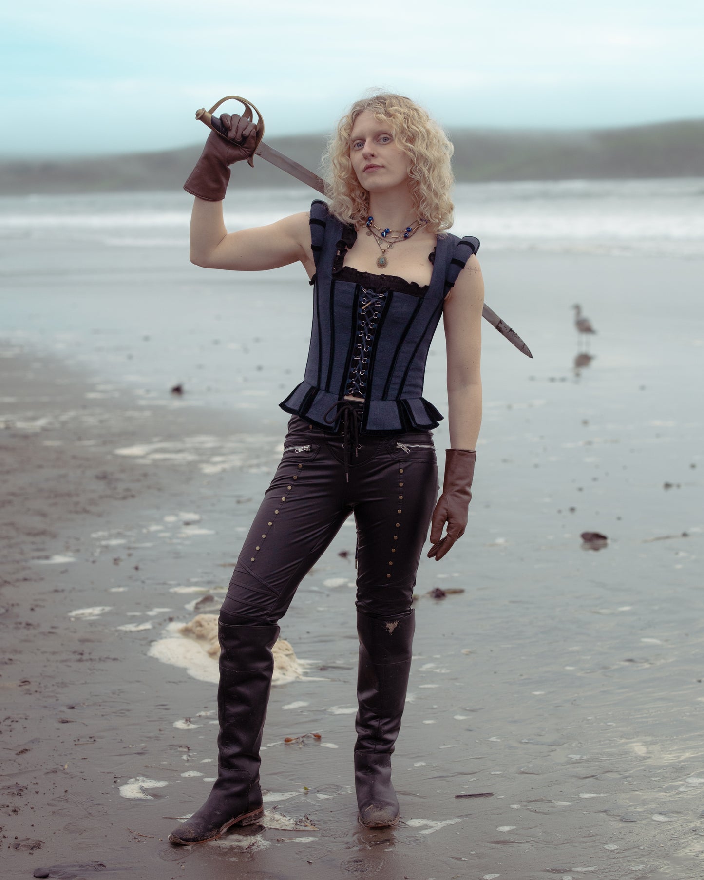 Person wearing Navy Tavern Bodice holding a sword standing on a beach with cloudy sky background