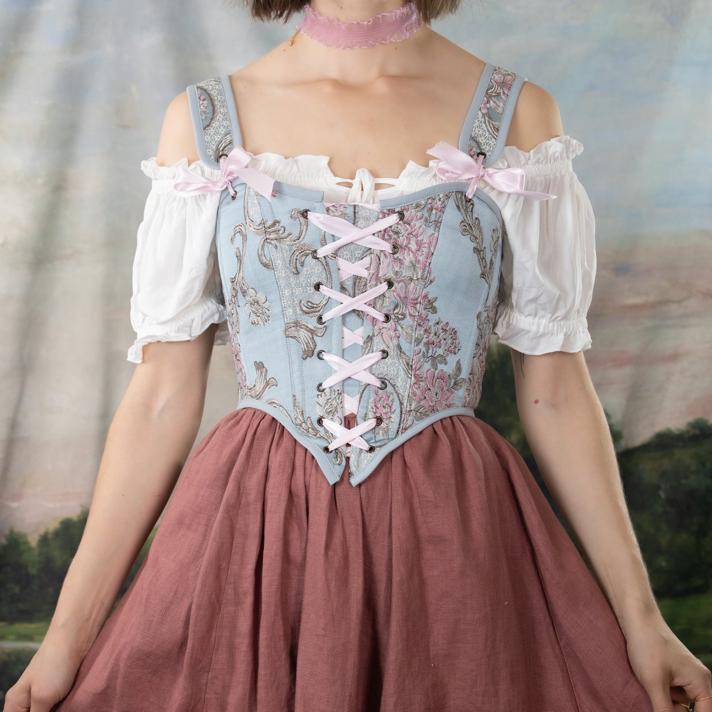 model wearing blue floral baroque corset with pink lacing ribbon