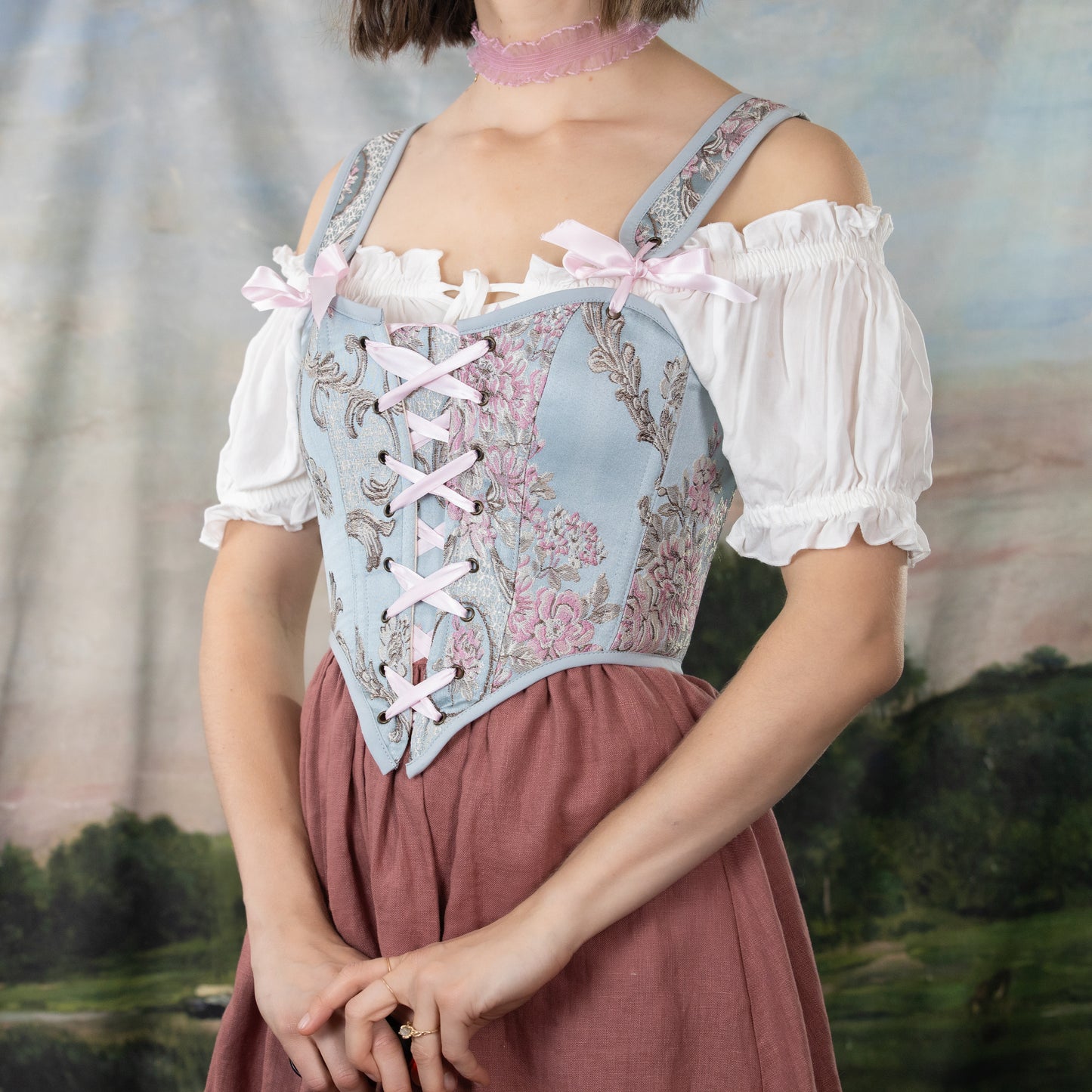 a brunette model wearing a blue corset with pink floral arrangements and a front lacing bodice style