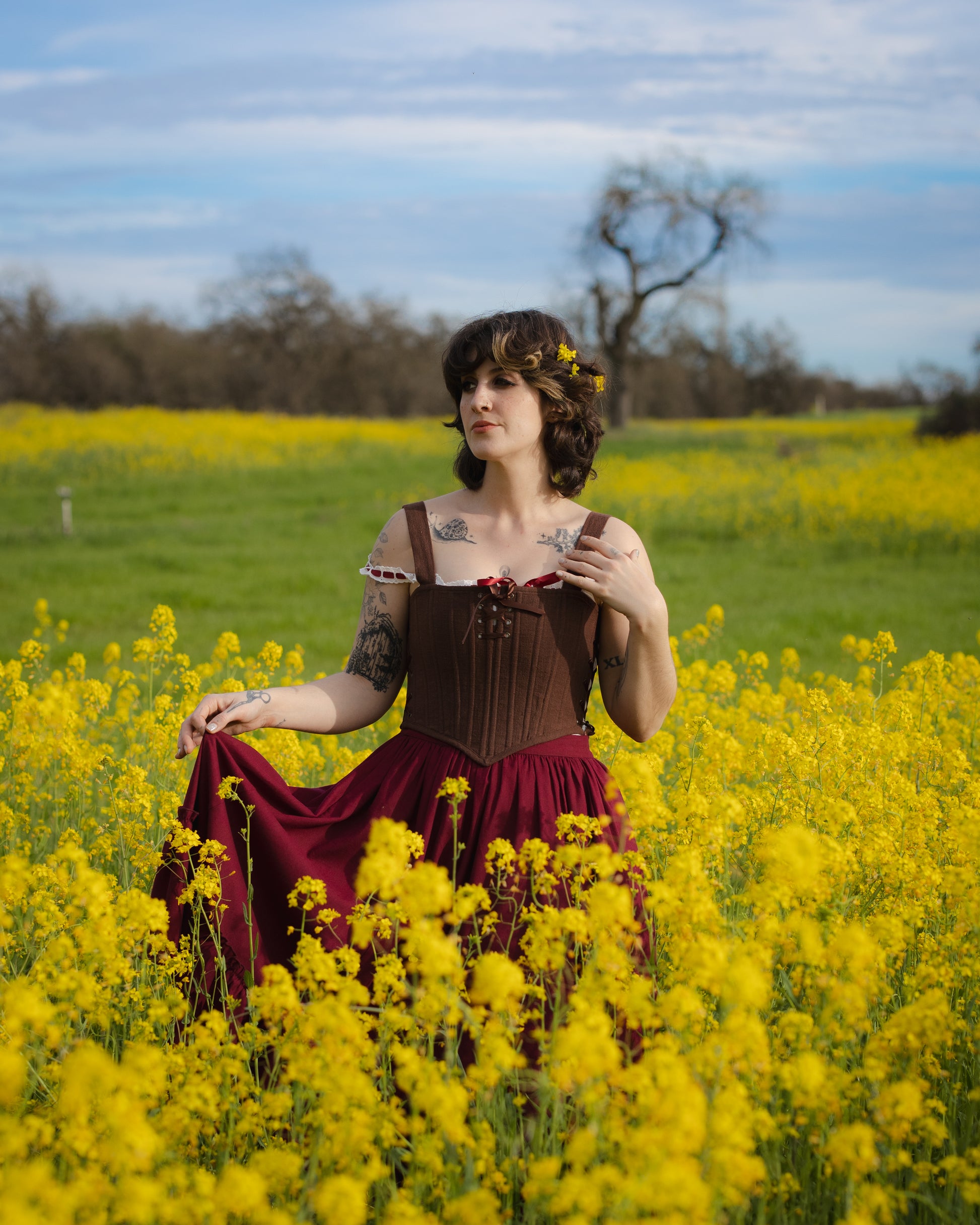 Woman wearing Brown Aurora Stays corset dress standing in a vibrant yellow flower field under a blue sky.