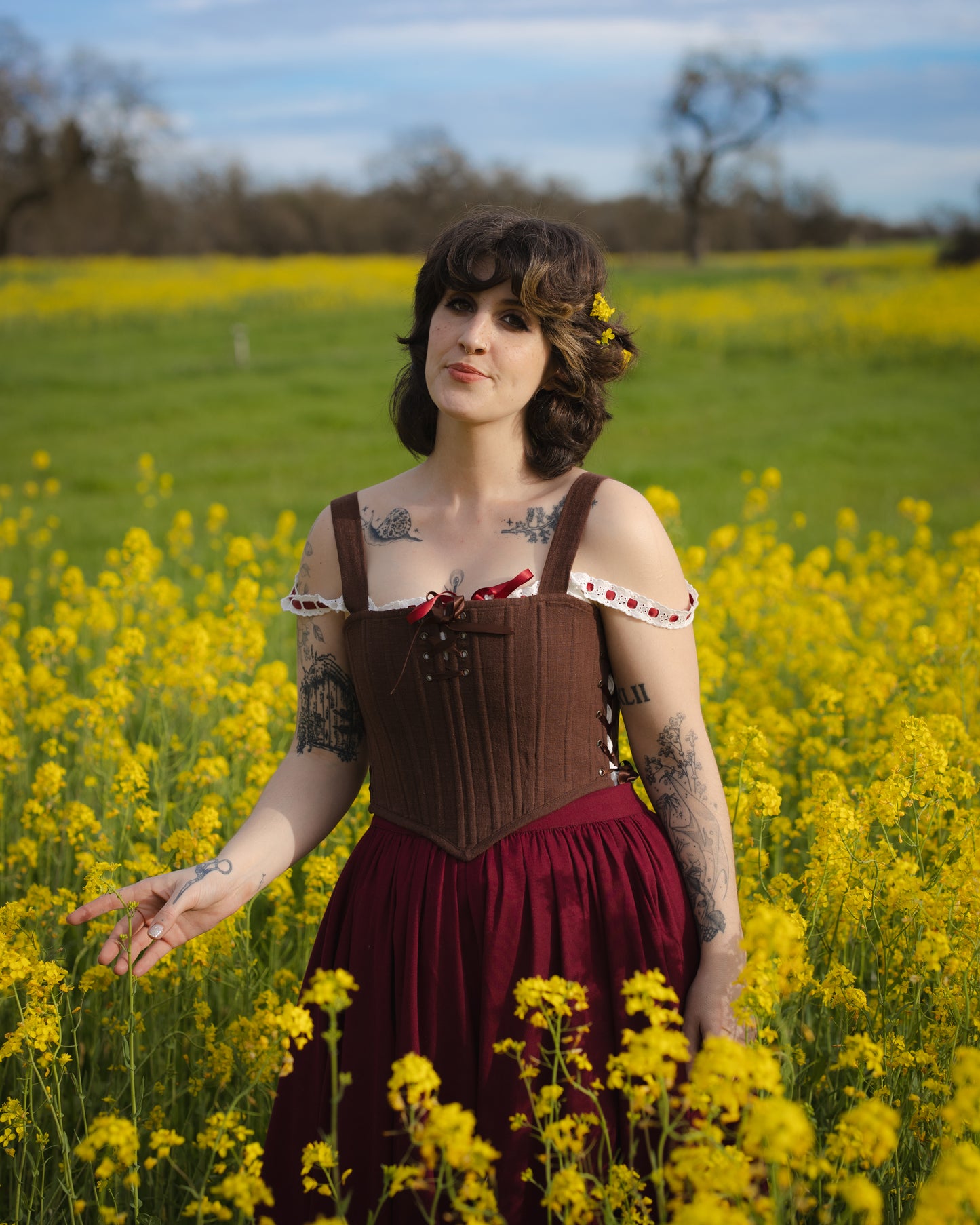 Woman wearing Brown Aurora Stays corset-style top with off-shoulder sleeves standing in a yellow flower field