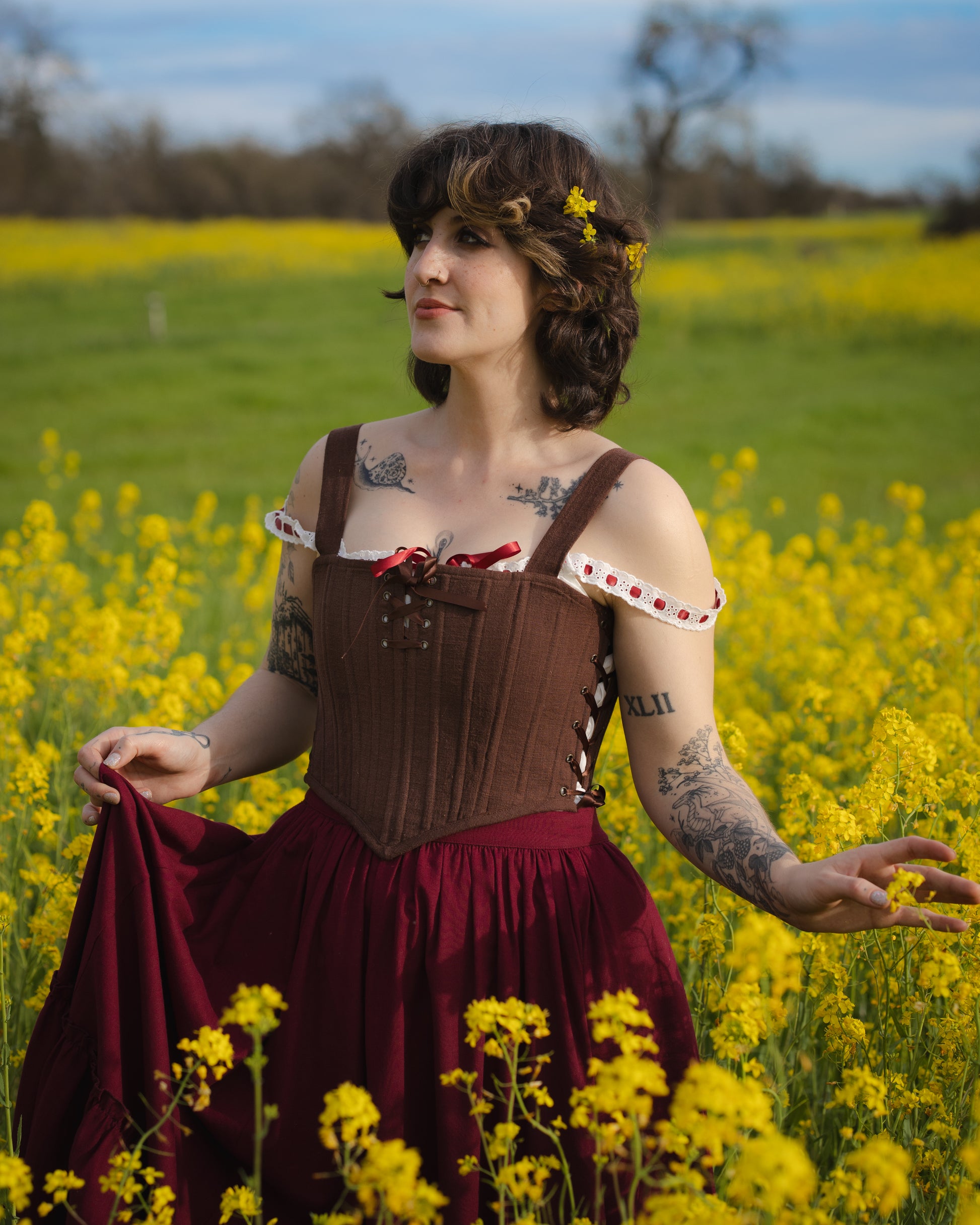 Woman wearing Brown Aurora Stays corset-style top standing in vibrant yellow flower field on sunny day