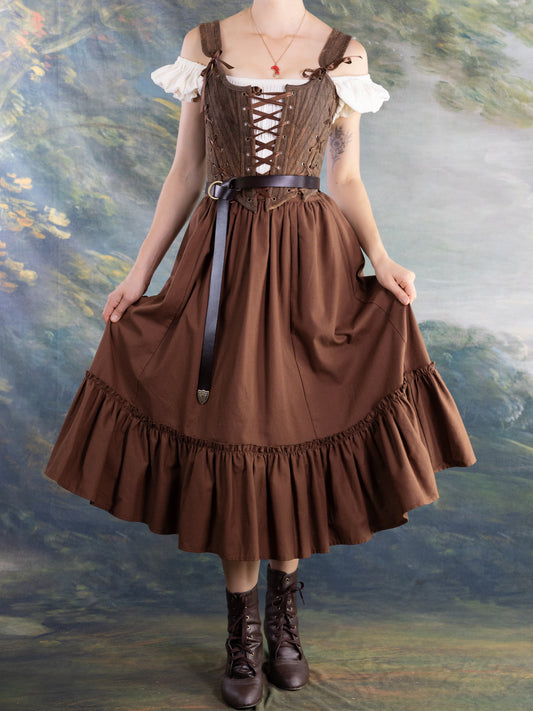 Woman wearing adjustable Brown Princess Stays corset with off-shoulder blouse and brown skirt against scenic backdrop