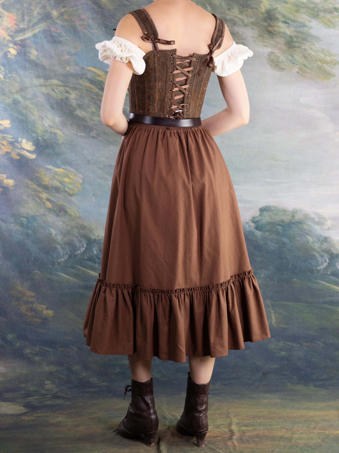 Back view of a woman wearing Brown Princess Stays corset styled with a brown skirt and vintage boots against painted backdrop