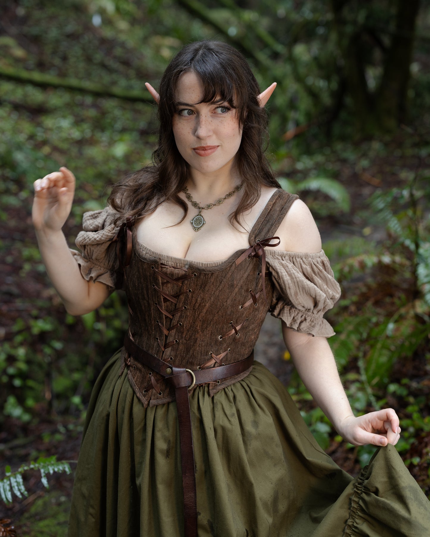 Woman in a forest wearing a Brown Milkmaid Dress with puff sleeves, corset bodice, and an olive green skirt.