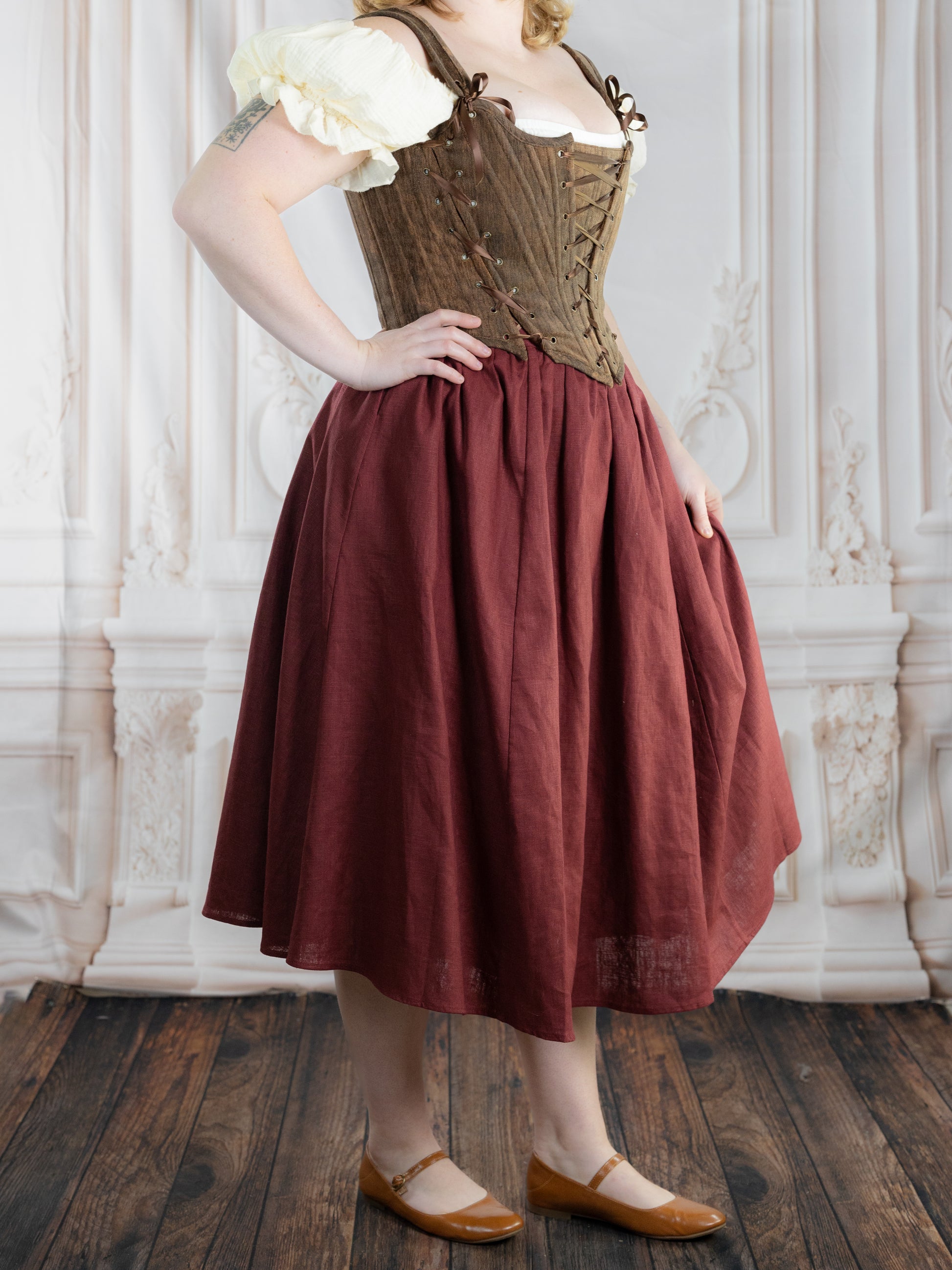 Woman wearing Brown Princess Stays corset with adjustable lacing paired with a red skirt and cream blouse in vintage setting
