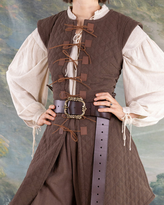 Woman wearing a brown Quilted Gambeson over a white blouse with a decorative belt around the waist