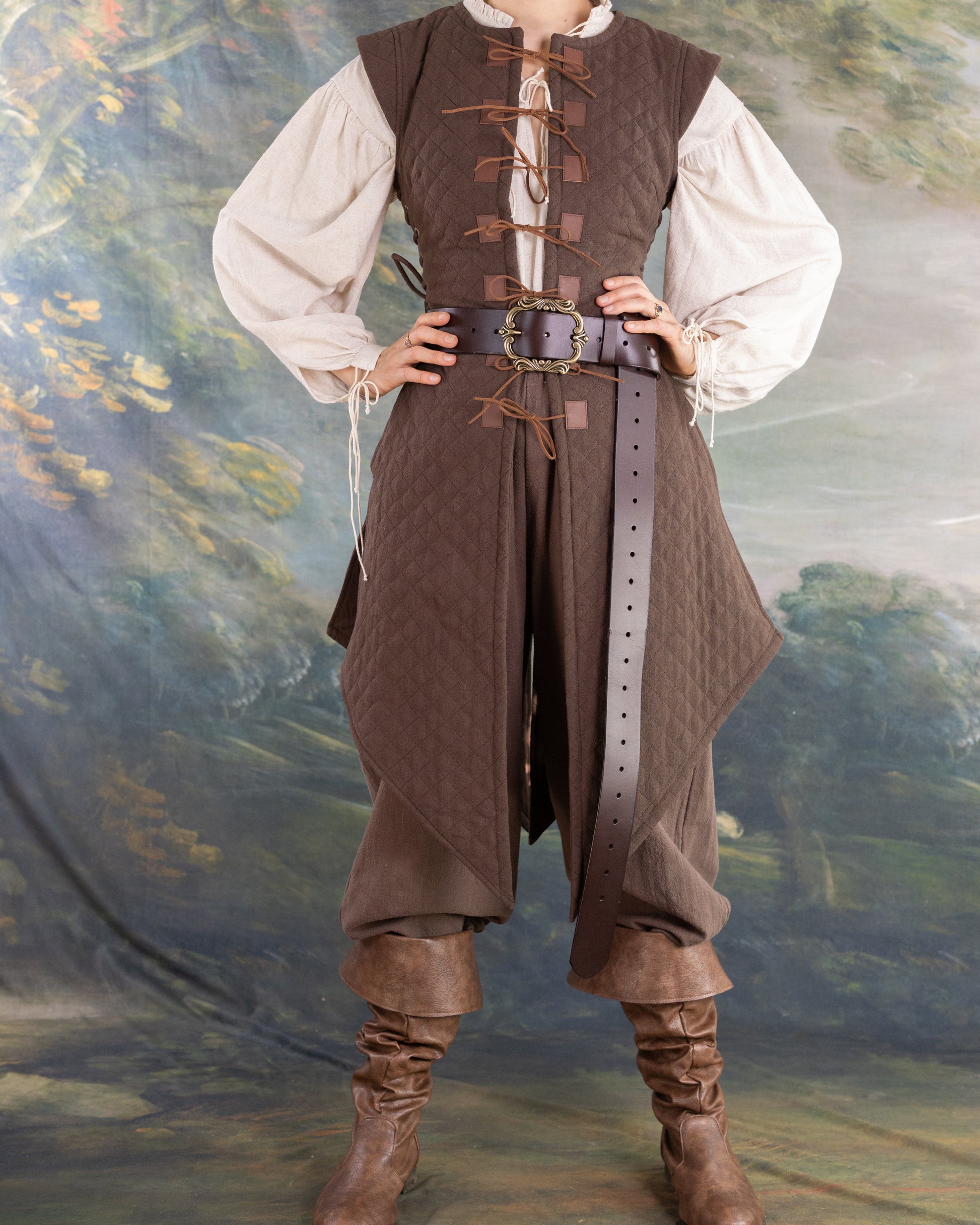 Front view of a brown Quilted Gambeson worn over a white blouse with brown pants and boots in a medieval style setting