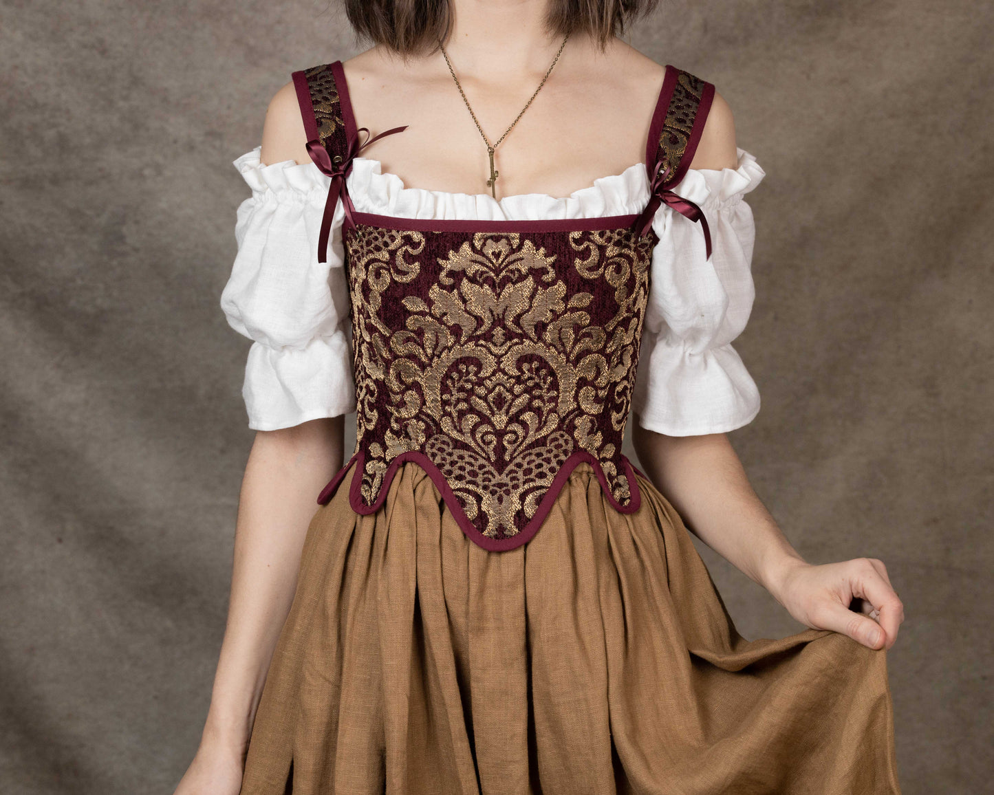 Woman wearing a Handmade Burgundy Chenille Tudor Stays corset over a white blouse and brown skirt, detailed gold pattern