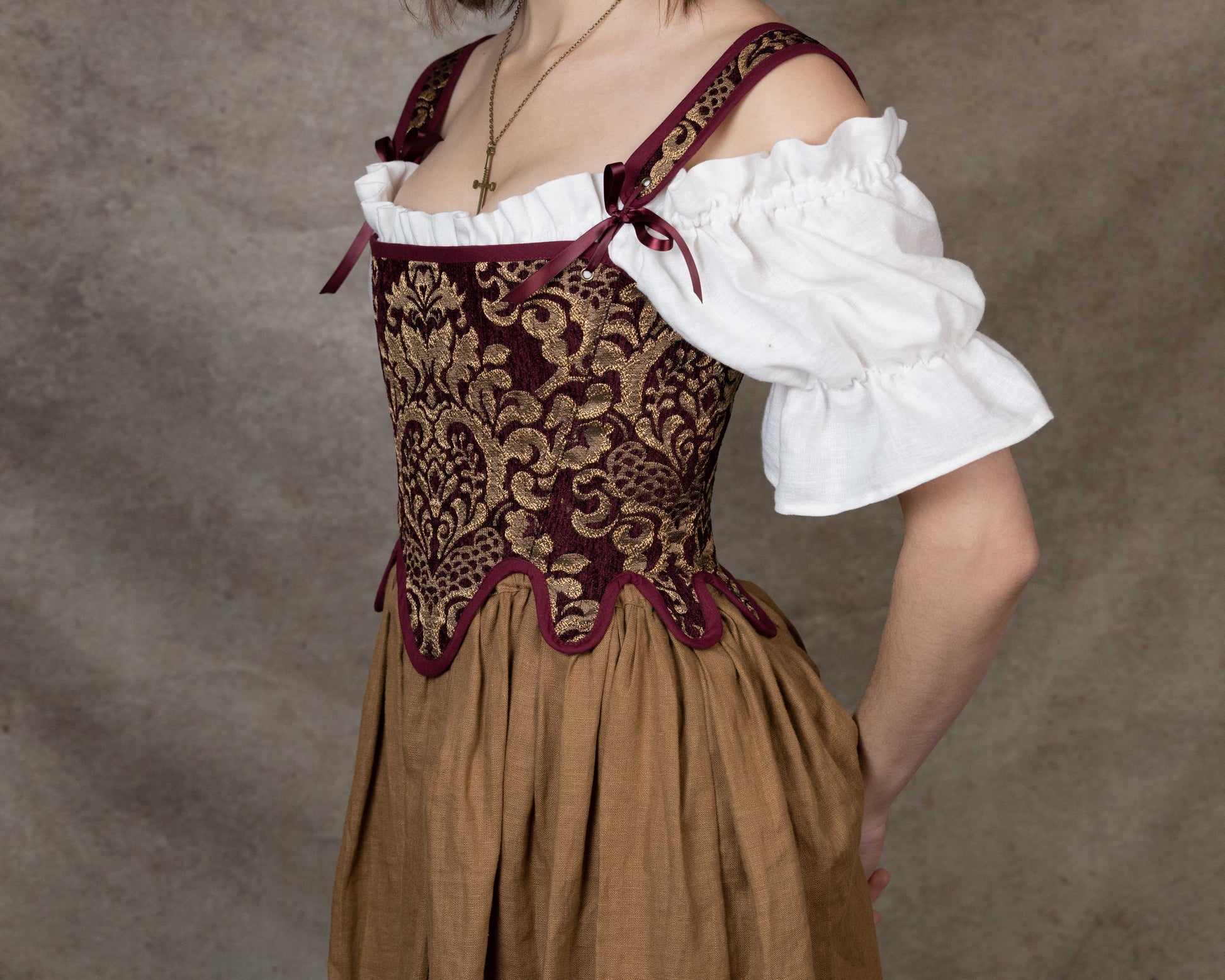 Handmade Burgundy Chenille Tudor Stays worn over a white ruffled blouse and brown skirt with intricate gold embroidery.