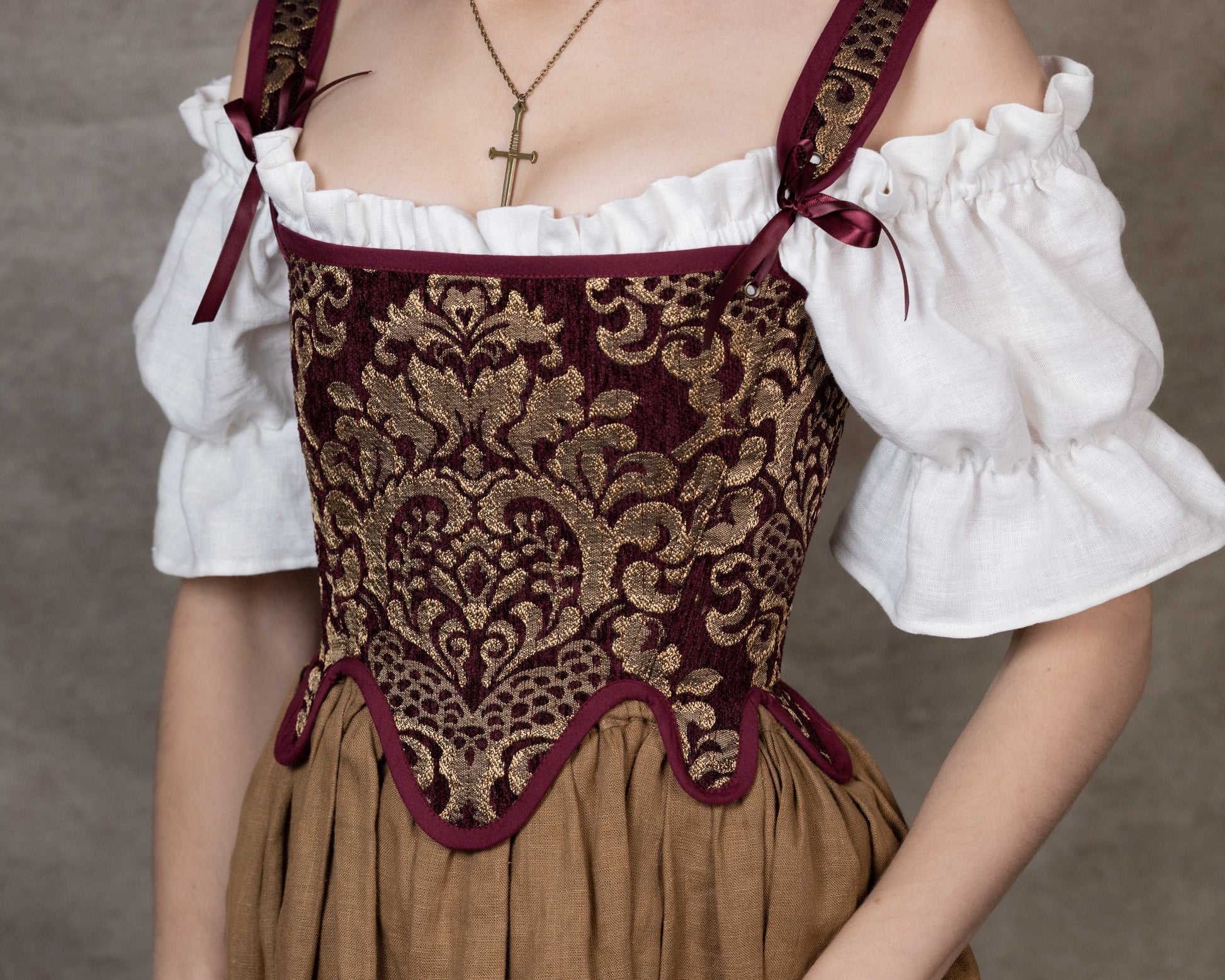 Close-up of a woman wearing Handmade Burgundy Chenille Tudor Stays with gold embroidery over a white blouse and brown skirt.