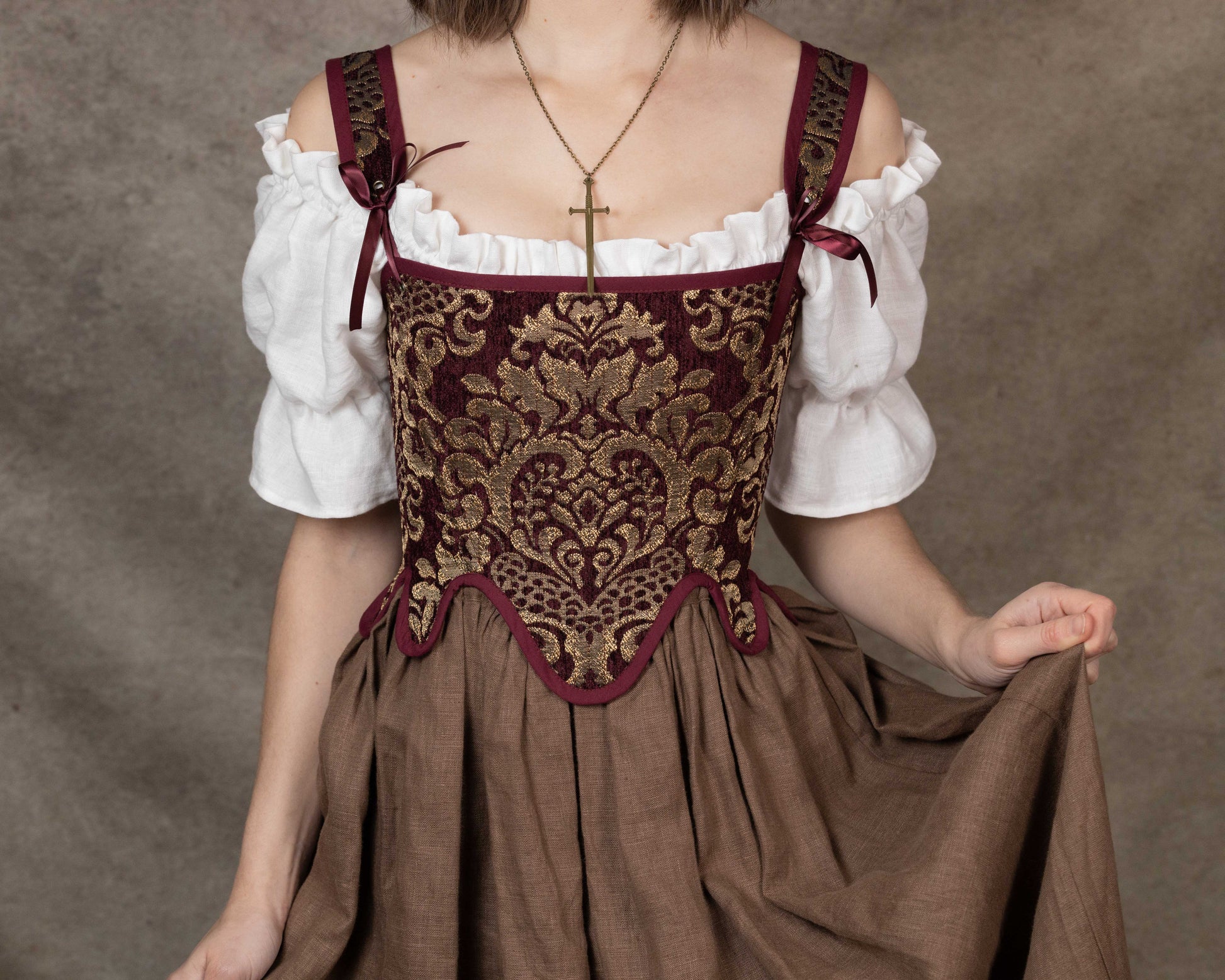 Woman wearing Handmade Burgundy Chenille Tudor Stays with intricate gold pattern over white blouse and brown skirt