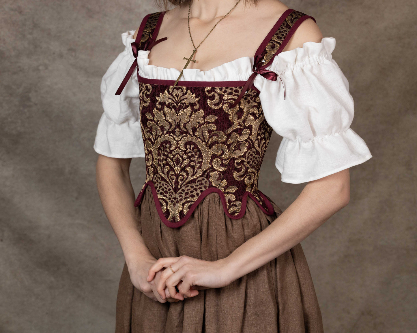 Woman wearing Handmade Burgundy Chenille Tudor Stays with intricate gold pattern over white blouse and brown skirt