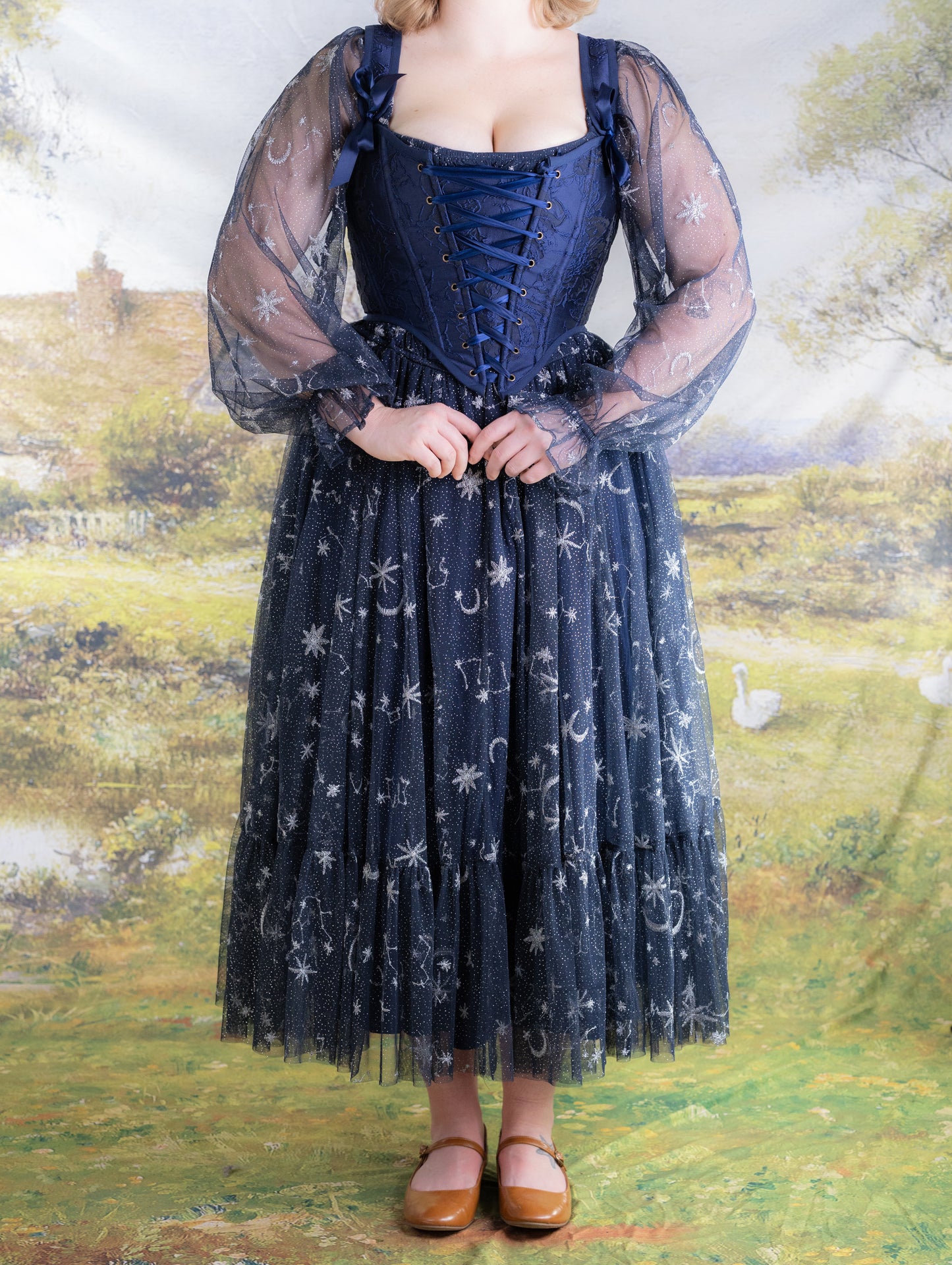 Woman wearing a dark blue floral jacquard corset with sheer celestial patterned sleeves and skirt standing outdoors