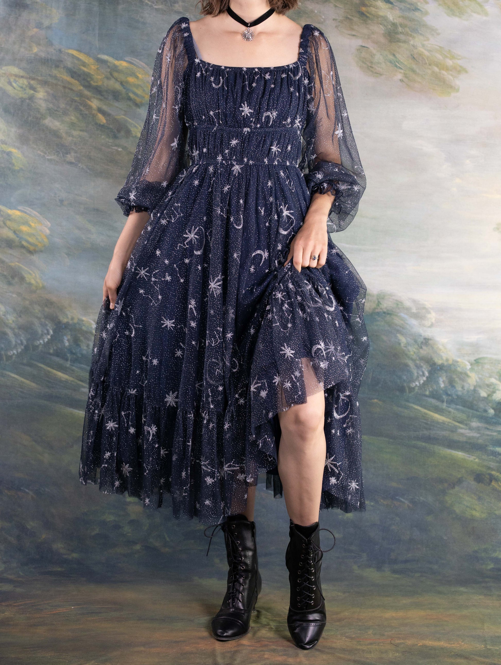 Woman wearing navy blue Celestial Tulle Dress with star patterns and sheer sleeves paired with black boots.