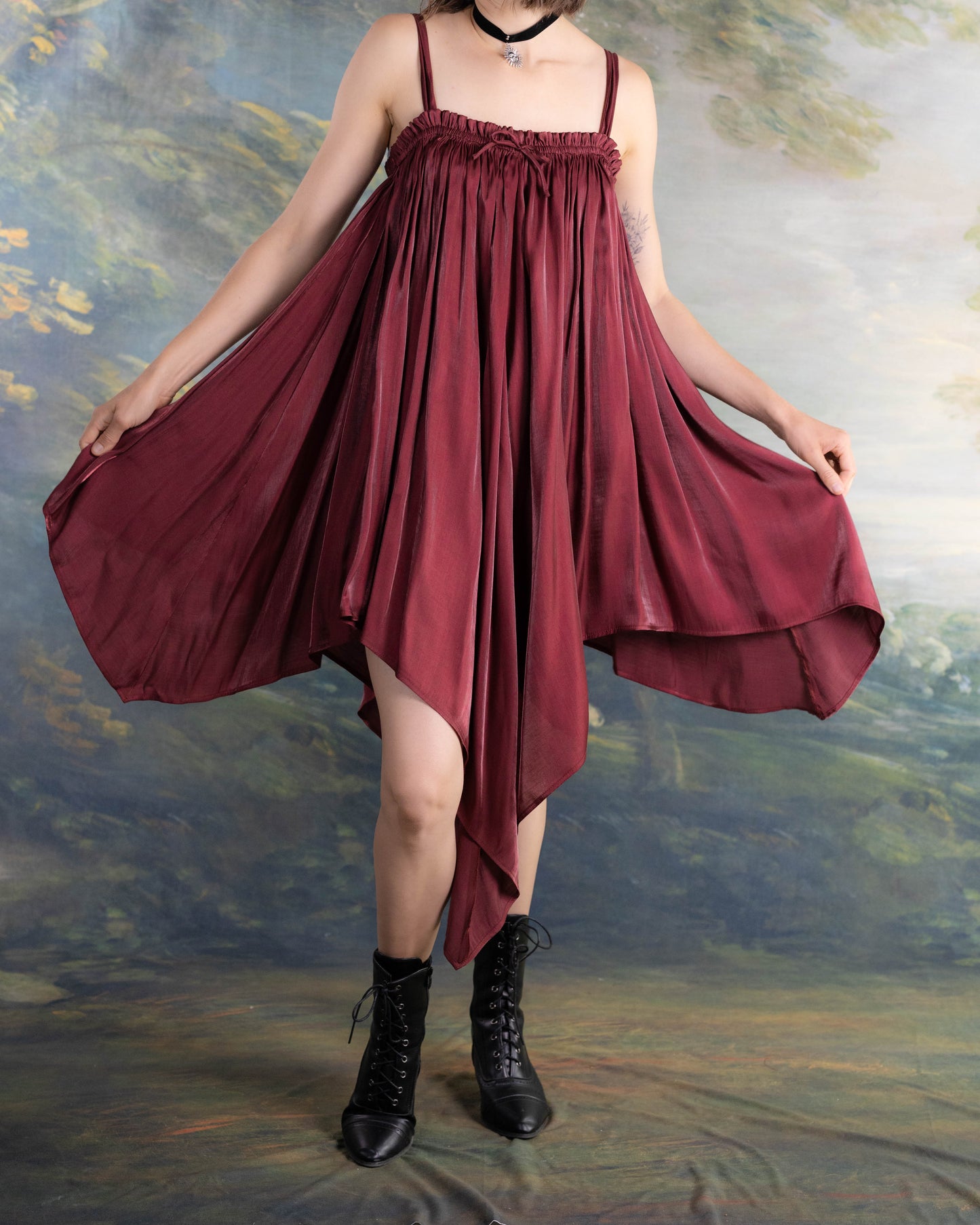 Woman wearing Dark Red Flutter Dress with handkerchief hem and flowing satin fabric paired with black boots