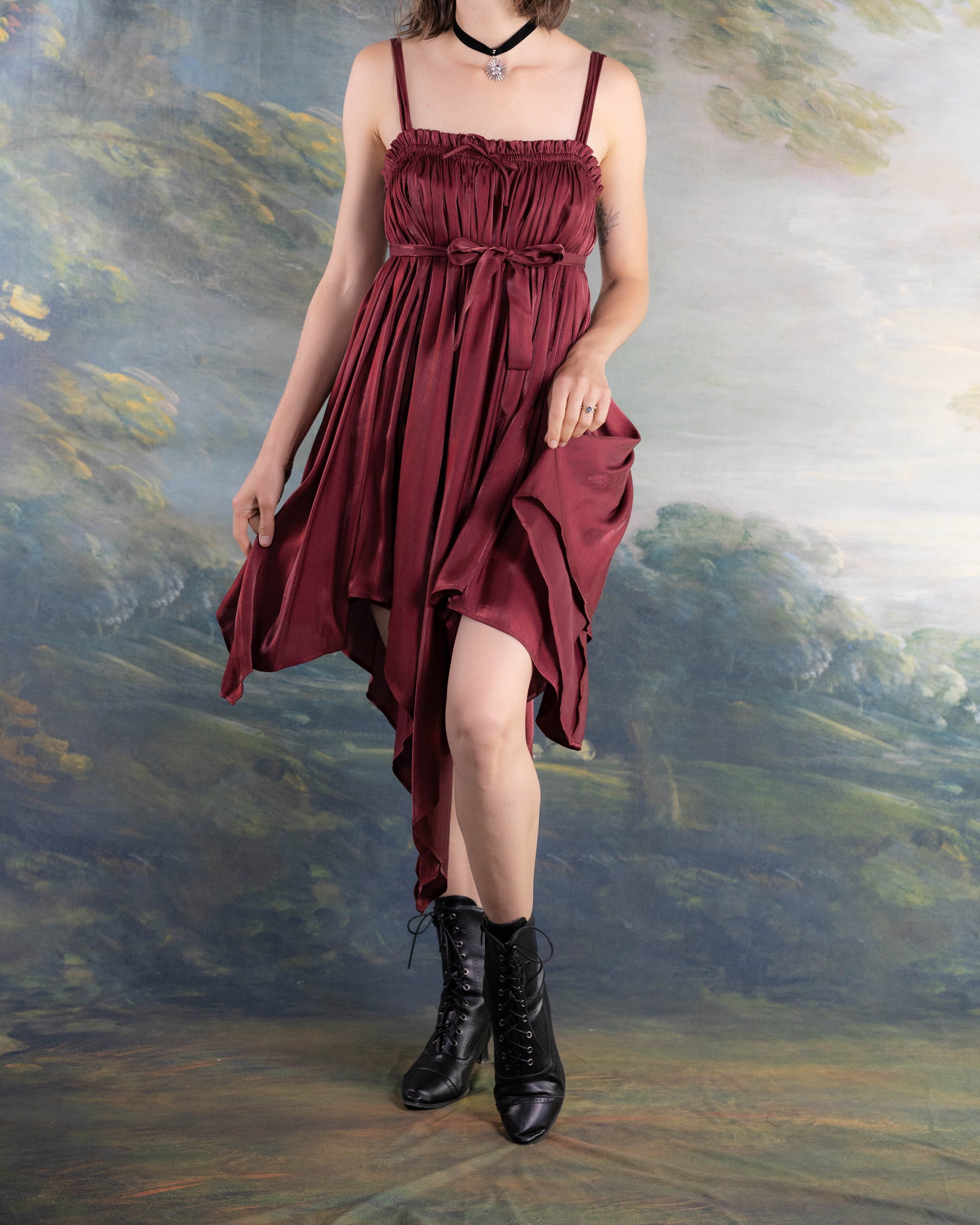 Woman wearing a Dark Red Flutter Dress with handkerchief hem and cinched waist paired with black lace-up boots