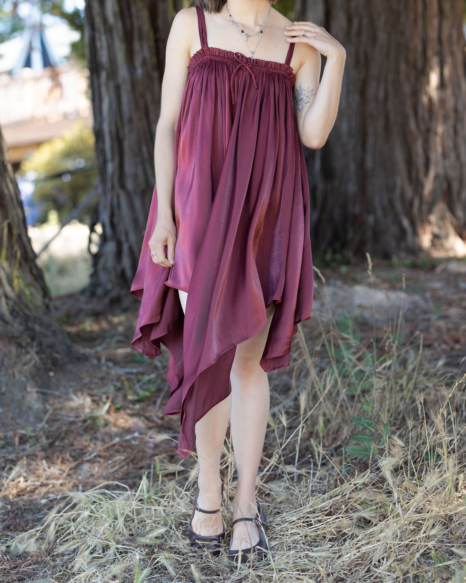 Woman wearing a Dark Red Flutter Dress with a flowing handkerchief hem standing outdoors near a large tree trunk