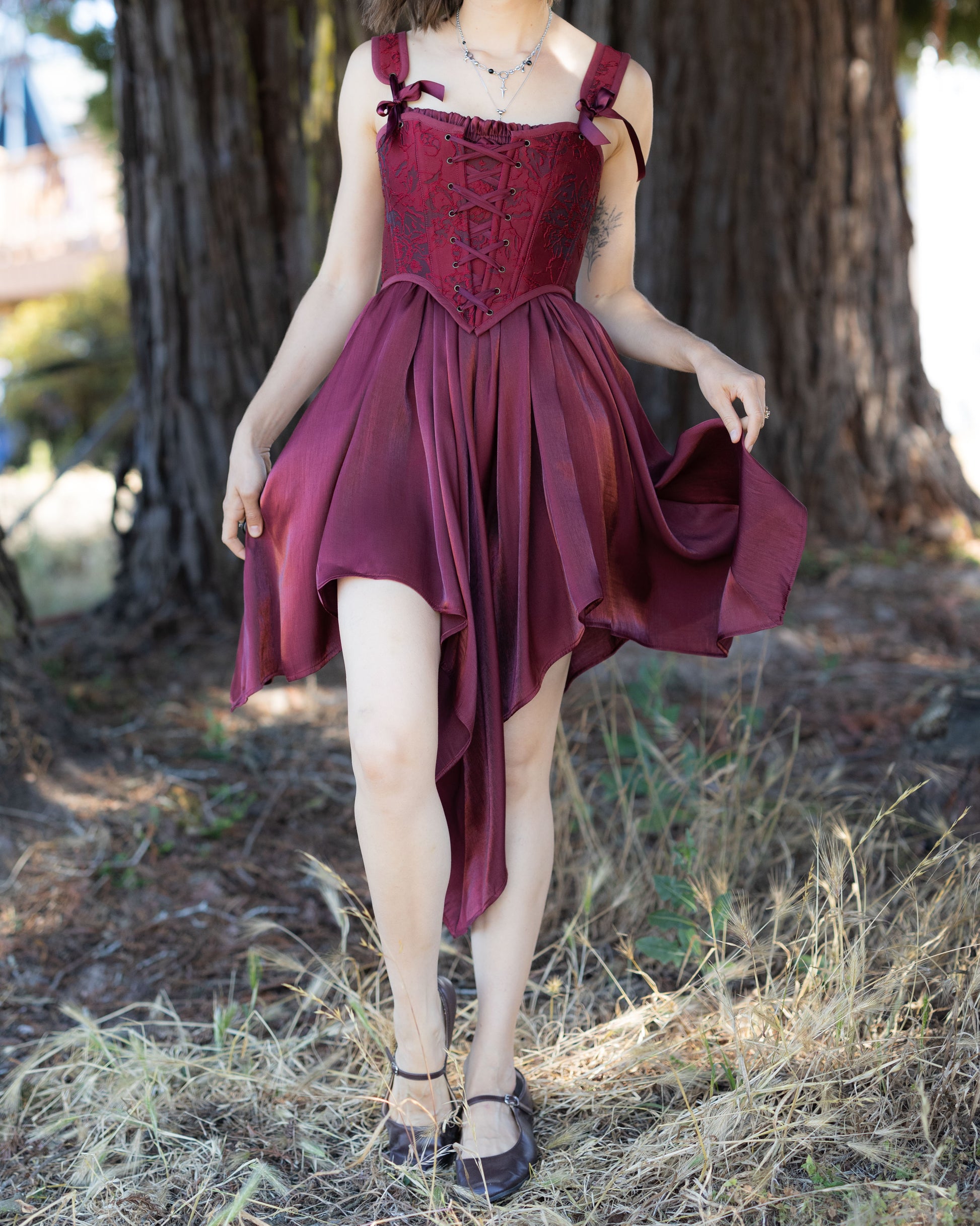 Woman wearing a flowing Dark Red Flutter Dress with handkerchief hem standing outdoors near a tree