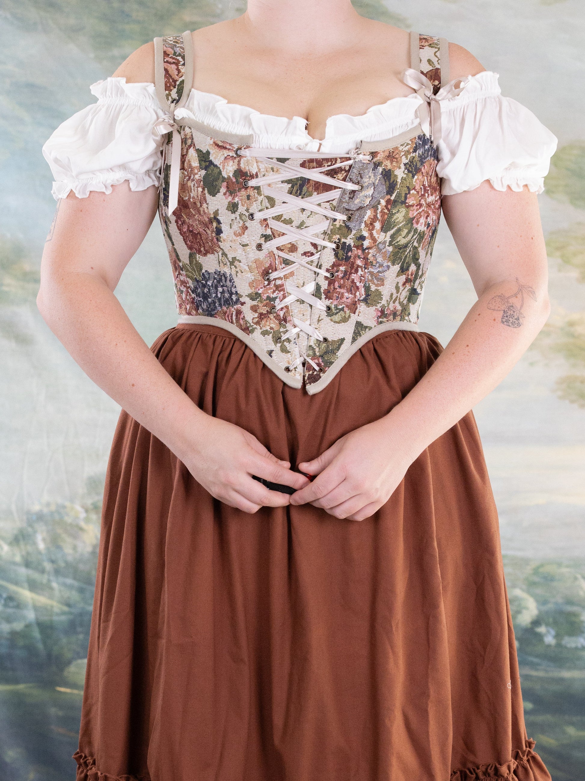 Woman wearing Floral Tapestry Corset with lace-up front over white off-shoulder blouse and rust-colored skirt in studio setting