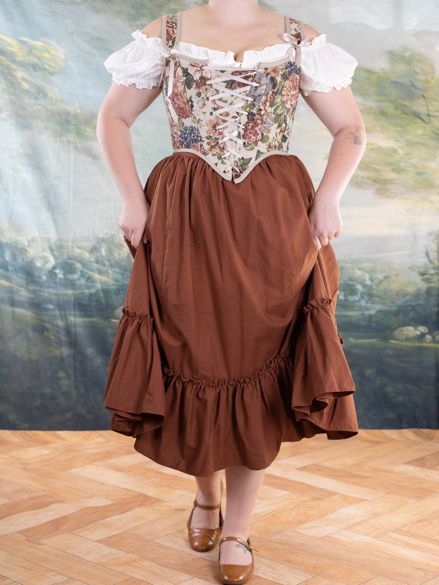 Woman wearing Floral Tapestry Corset with white off-shoulder blouse and rust-colored skirt in indoor studio setting