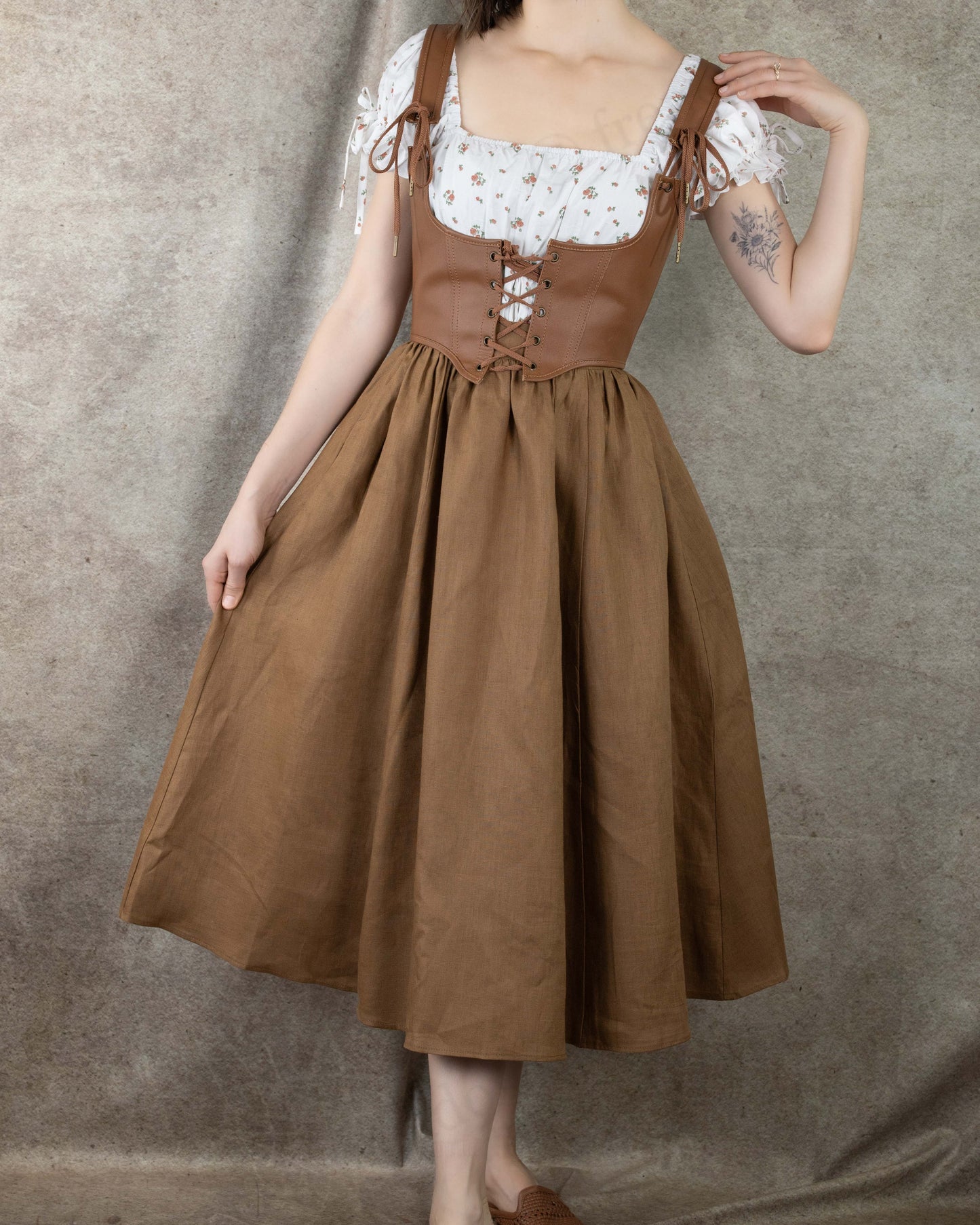 model wearing cute cottagecore outfit consisting of leather underbust corset layered over a white milkmaid dress and brown midi skirt