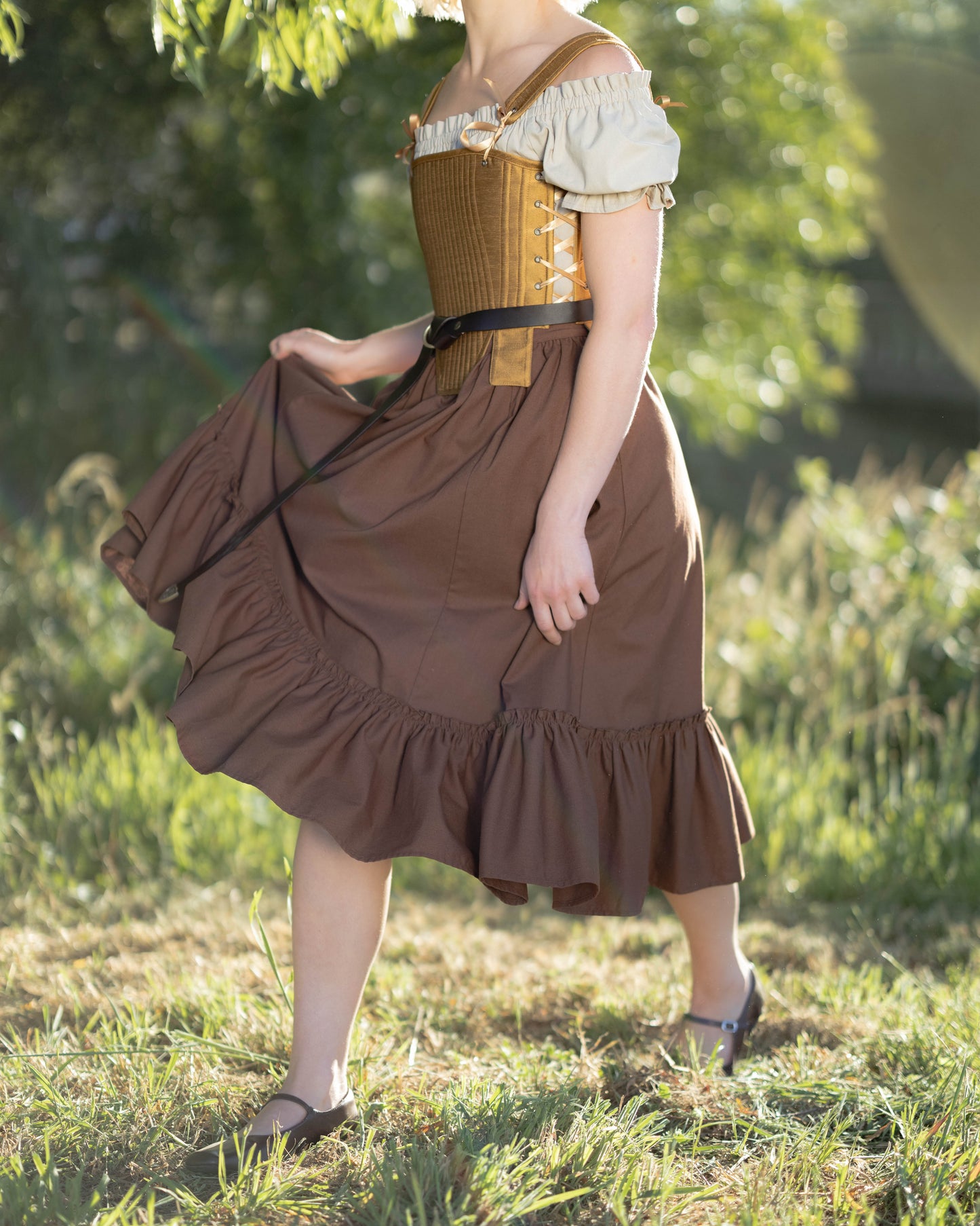Woman in a brown dress with off-shoulder white top walking through sunlit grassy area outdoors