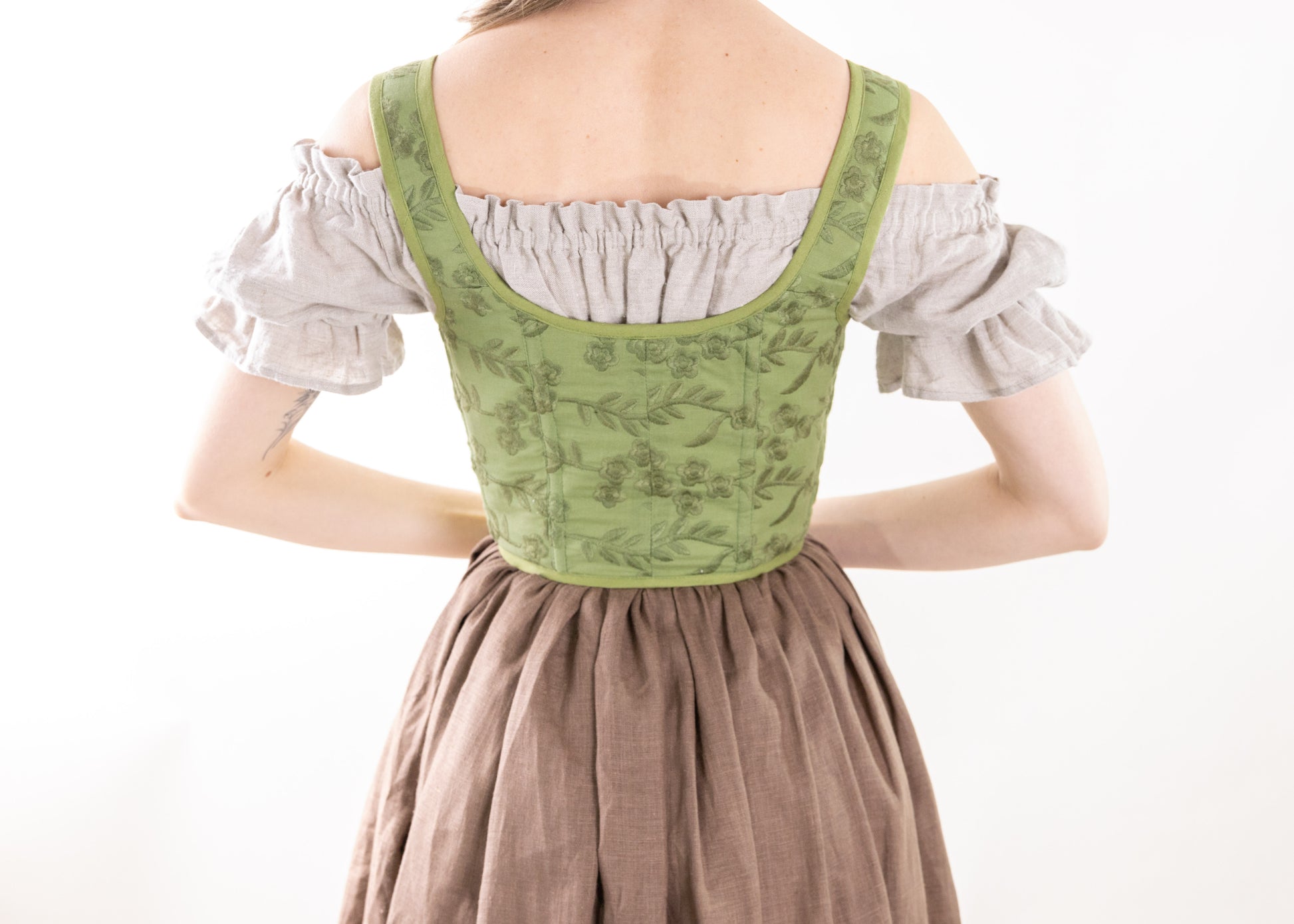 Back view of a woman wearing a Handmade Moss Green Embroidered Floral Corset over a beige blouse and brown skirt