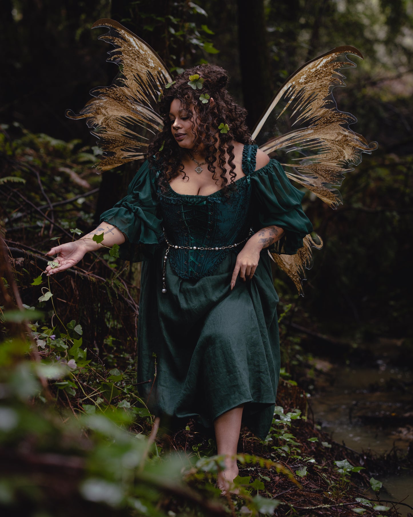 A woman in Dark Green Floral Jacquard 18th Century Stays with golden fairy wings in a lush forest setting.