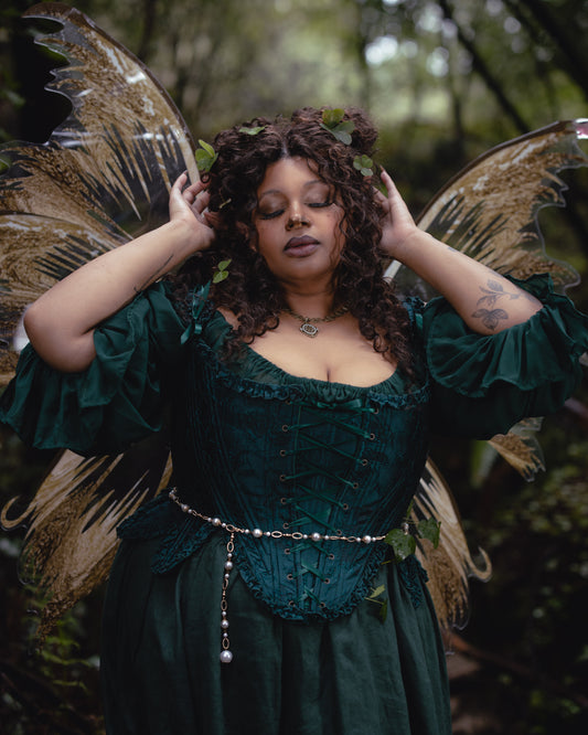 Woman wearing Dark Green Floral Jacquard 18th Century Stays with curly hair and decorative greenery in a forest setting