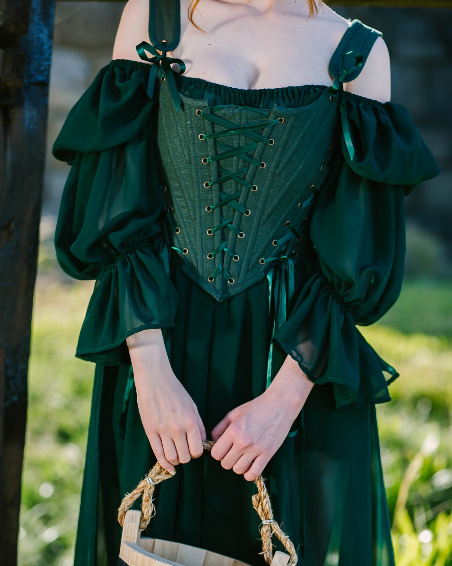Close-up of a woman wearing Forest Green Princess Stays corset with flowing off-shoulder sleeves outdoors in soft light