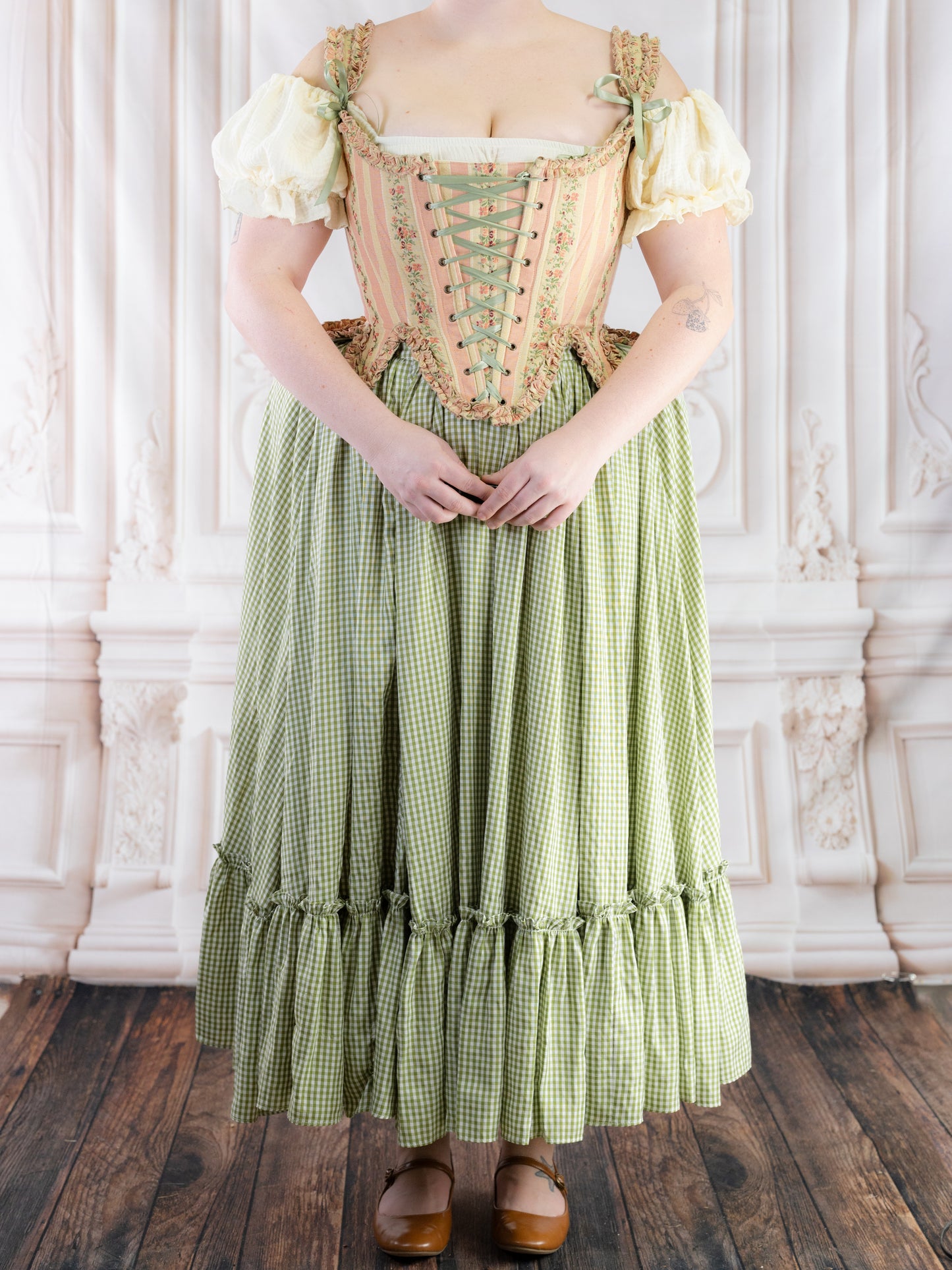 Woman wearing a vintage style dress with a Green Gingham Ruffle Skirt standing on wooden floor in ornate room
