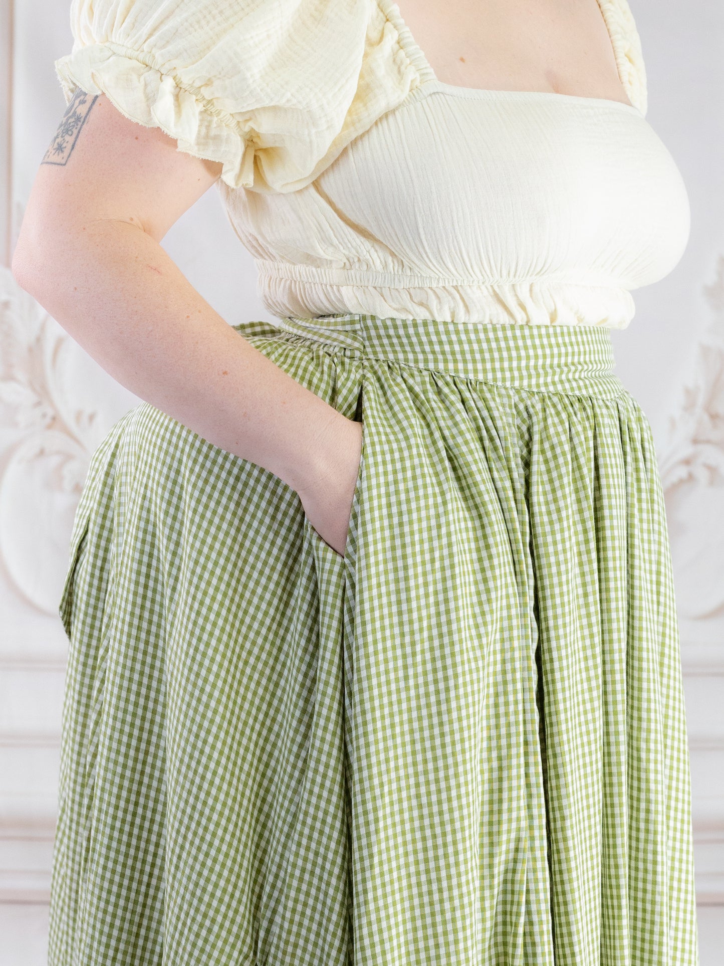 Close-up of a person wearing a Green Gingham Ruffle Skirt with a cream puff sleeve top, hand in pocket