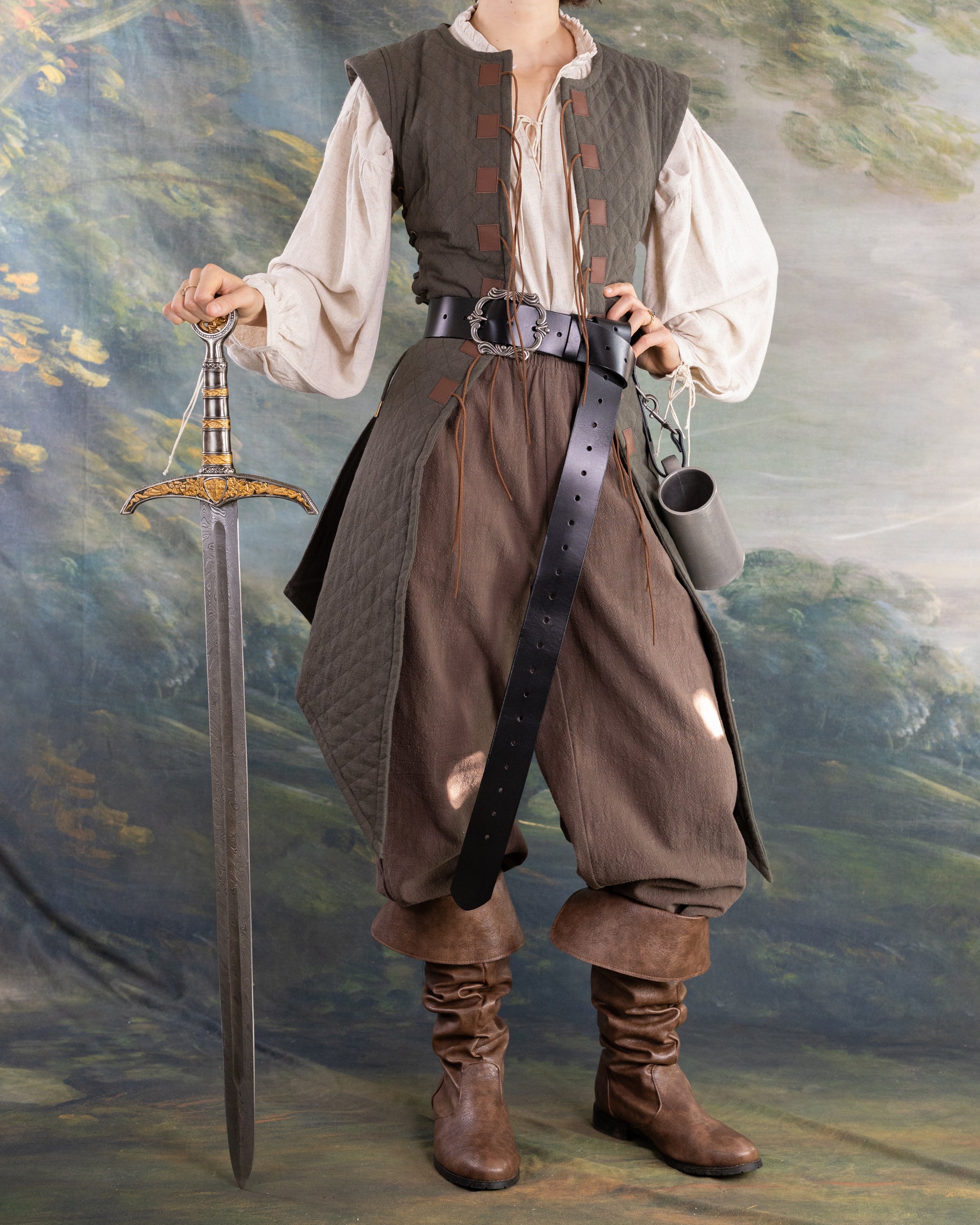 Woman wearing Quilted Gambeson with medieval sword and leather boots against painted backdrop