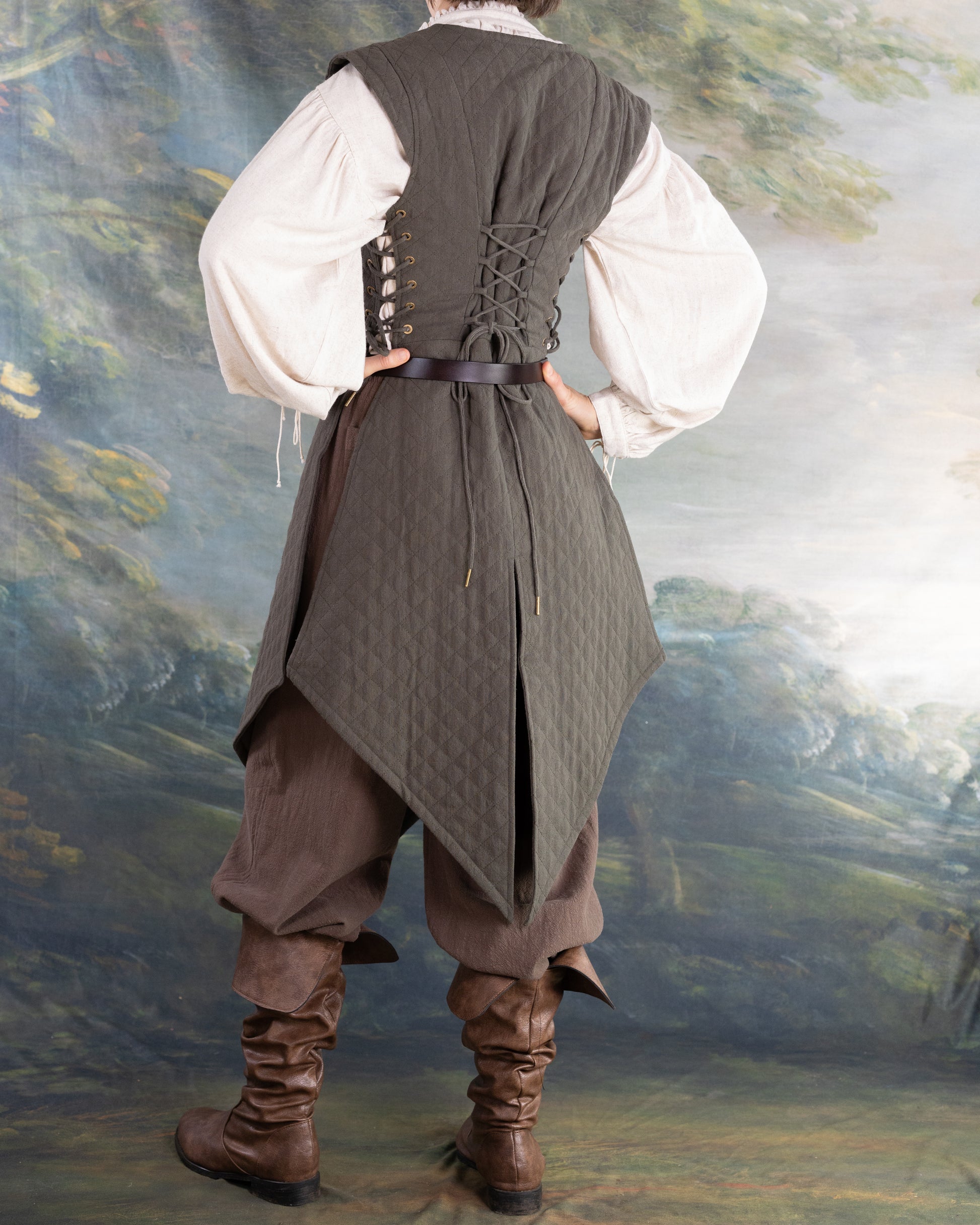 Back view of a woman wearing a brown quilted gambeson with lace-up sides and a belted waist over medieval style clothing.