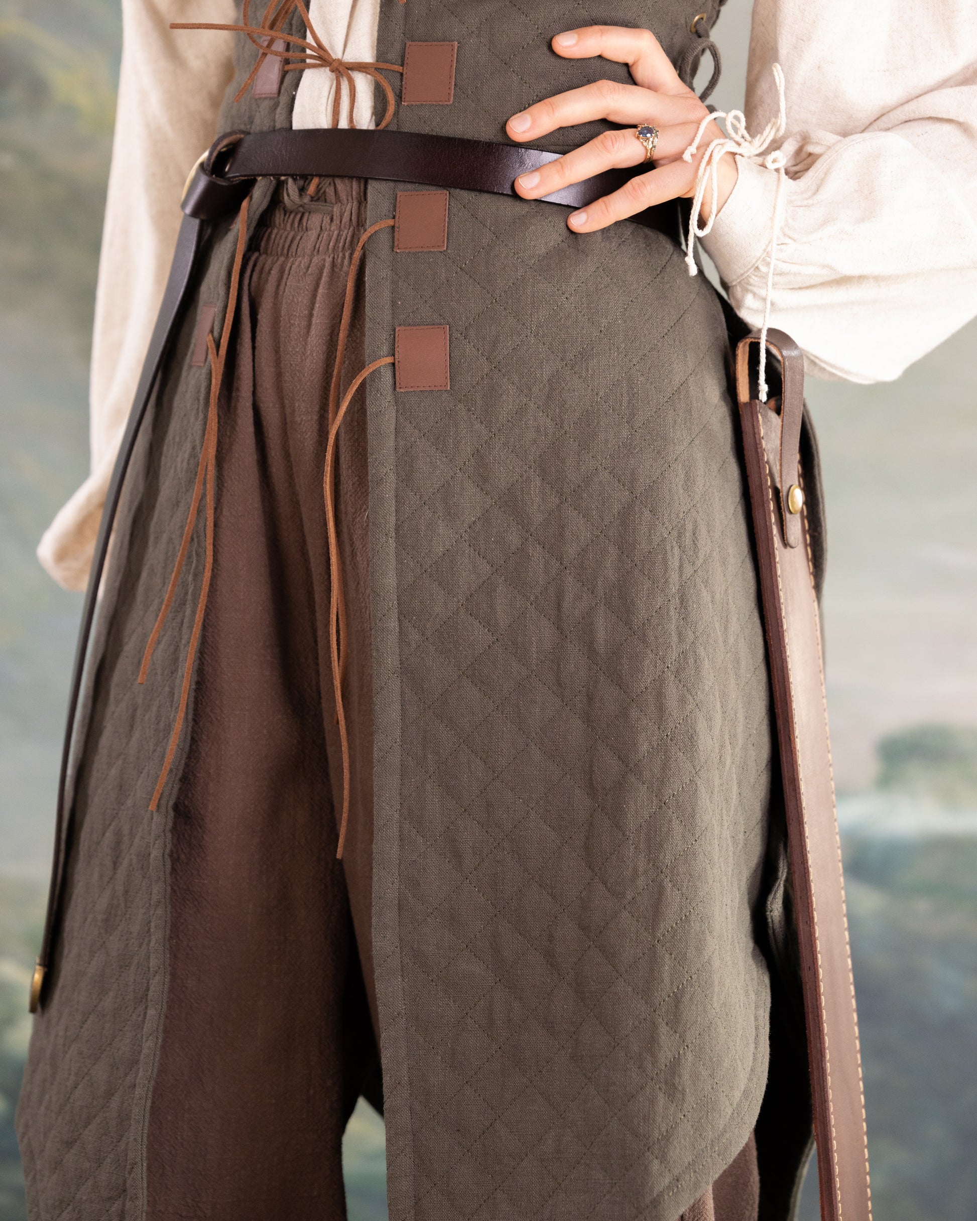 Close-up of a woman wearing a brown quilted gambeson with leather belt and historical inspired design details
