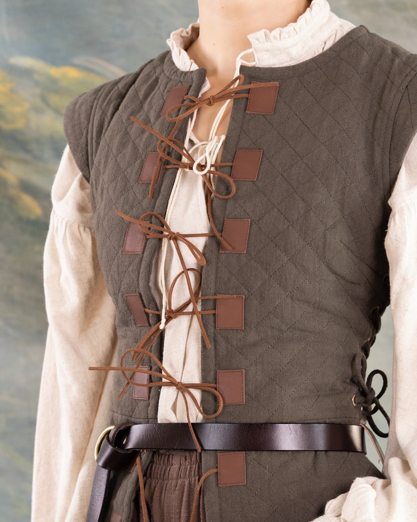 Close-up of a person wearing a dark brown Quilted Gambeson with leather ties and belt over a cream blouse