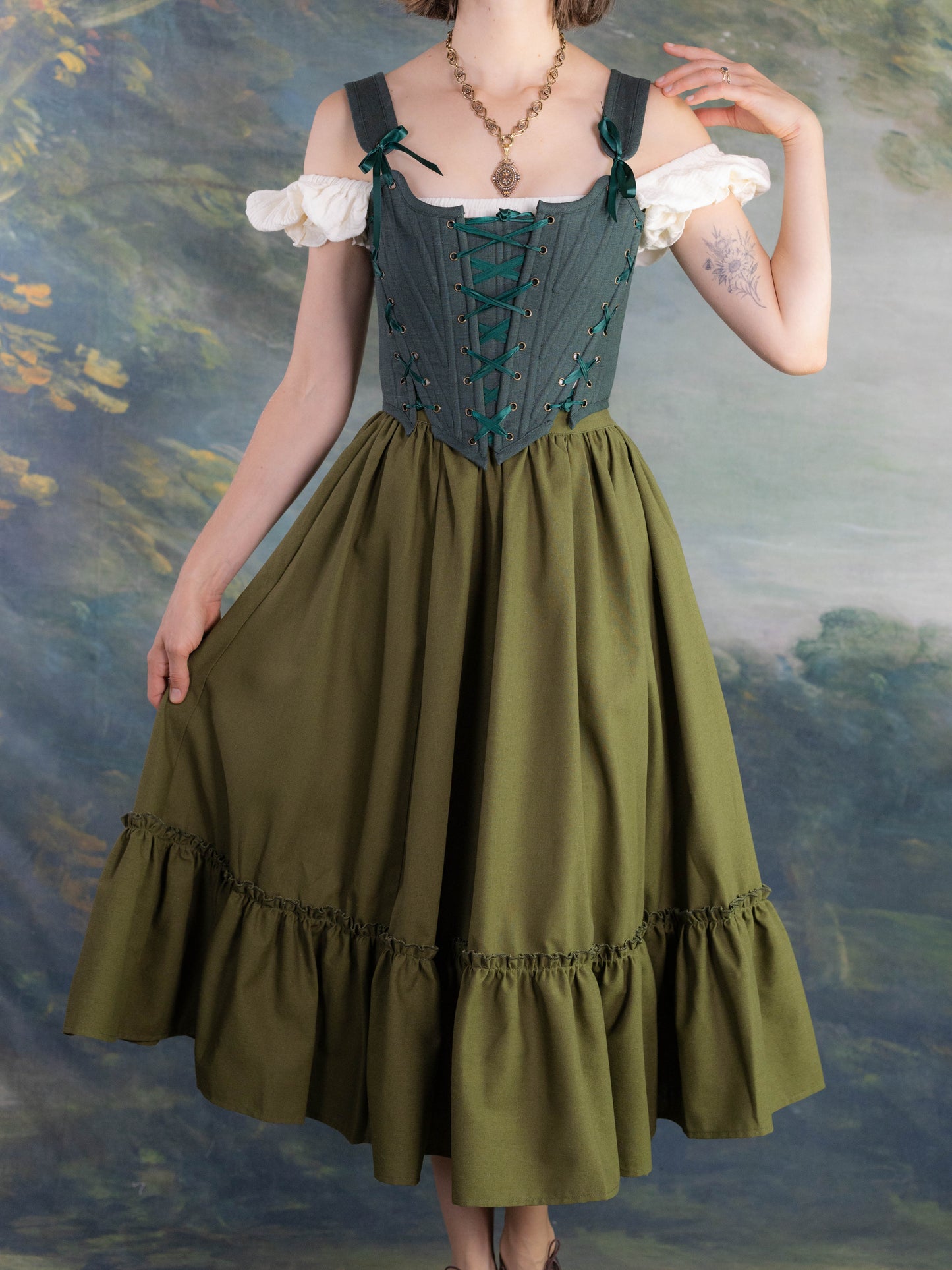 Woman wearing Forest Green Princess Stays corset with off-shoulder white blouse and flowing green skirt in vintage setting