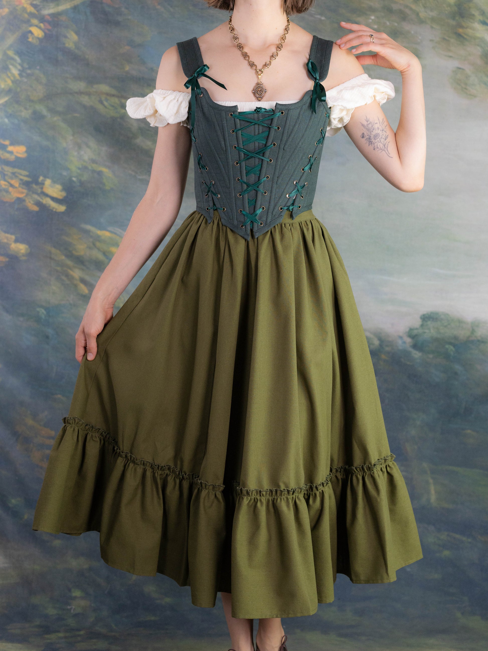Woman wearing Forest Green Princess Stays corset with off-shoulder white blouse and flowing green skirt in vintage setting