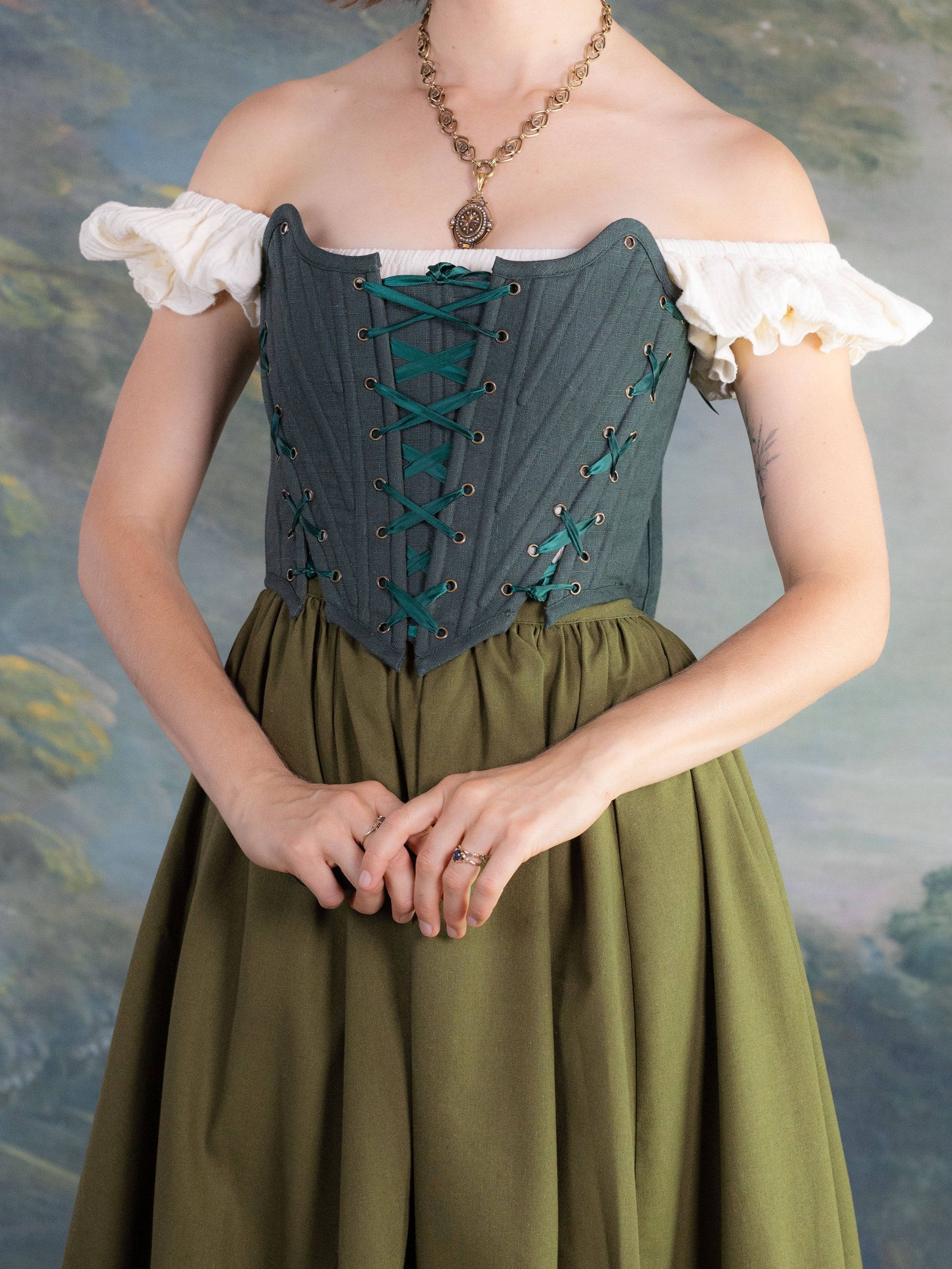 Woman wearing a Forest Green Princess Stays corset with lace-up front and vintage-inspired style over white blouse and green skirt